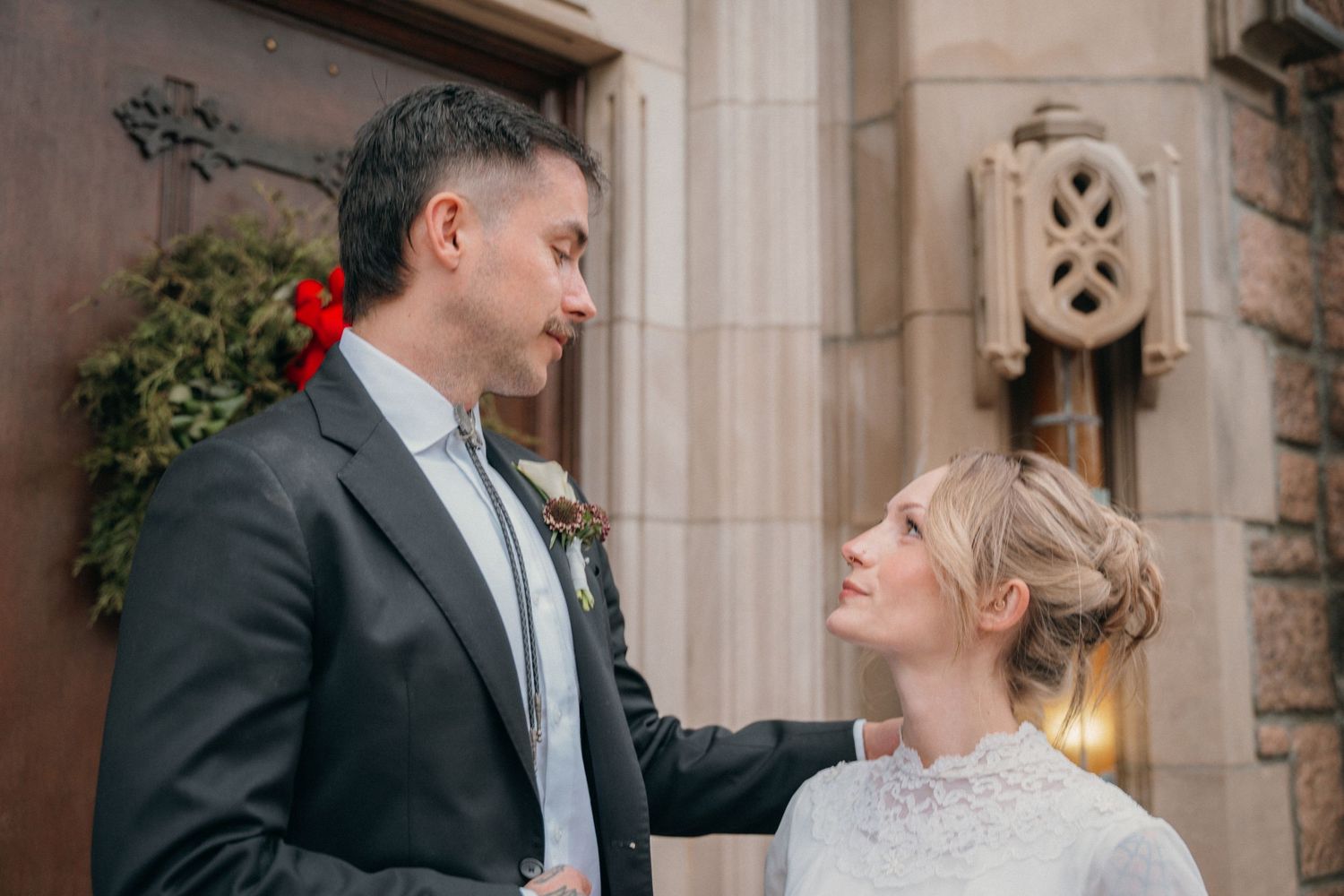 Groom looking down at his bride outside a church decorated for Christmas