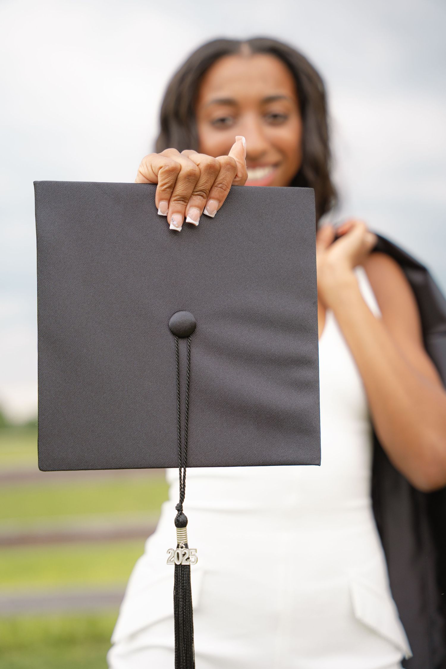 Graduate holding up her graduation cap and tassel in a white dress