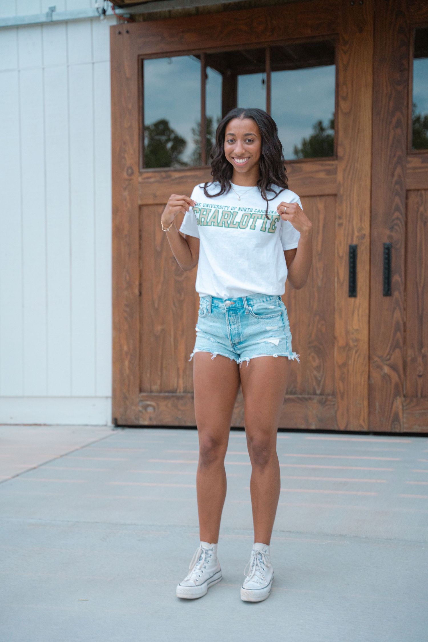 Senior portrait of a graduate in a Charlotte T-shirt standing before wooden barn doors