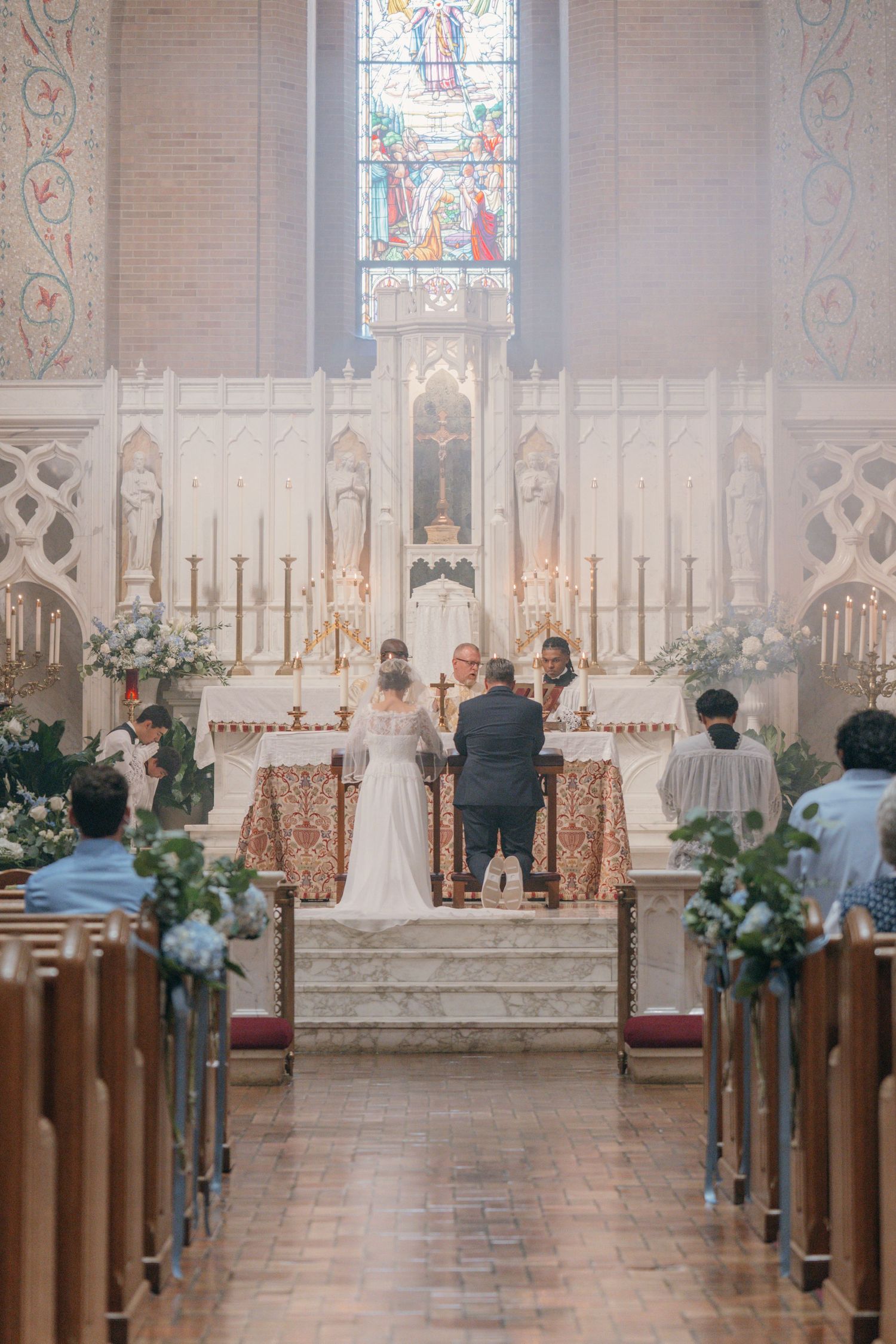 Bride and groom at the altar seen down the aisle of a church with stained glass