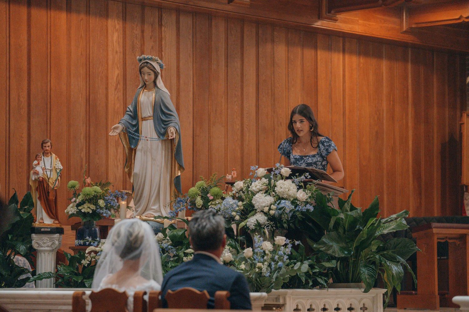Couple praying before a statue of the Virgin Mary surrounded by flowers