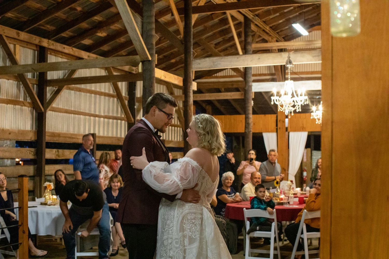 Bride and groom dancing in a timber barn surrounded by reception tables