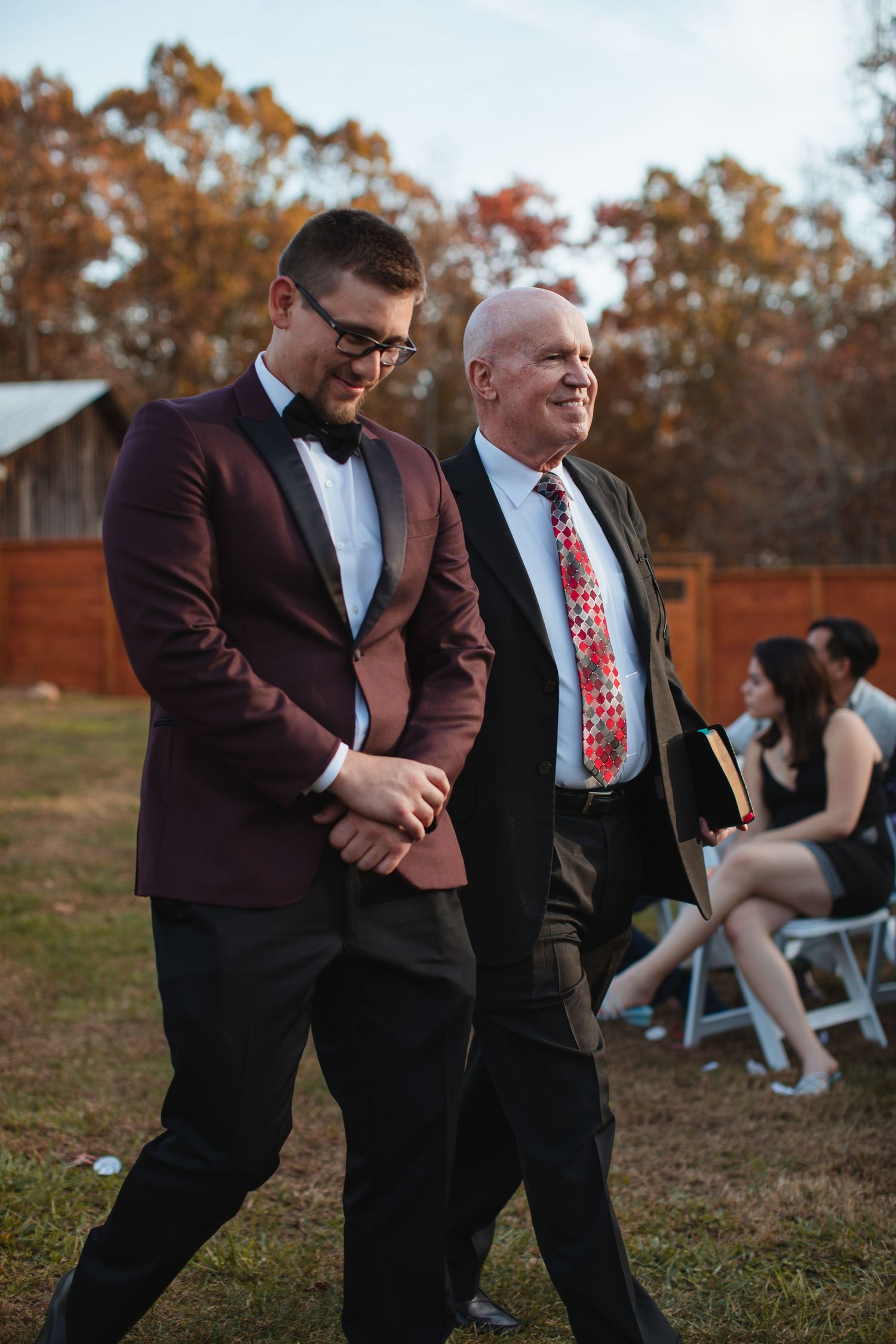 Groom in a burgundy jacket walking down the aisle with a family member