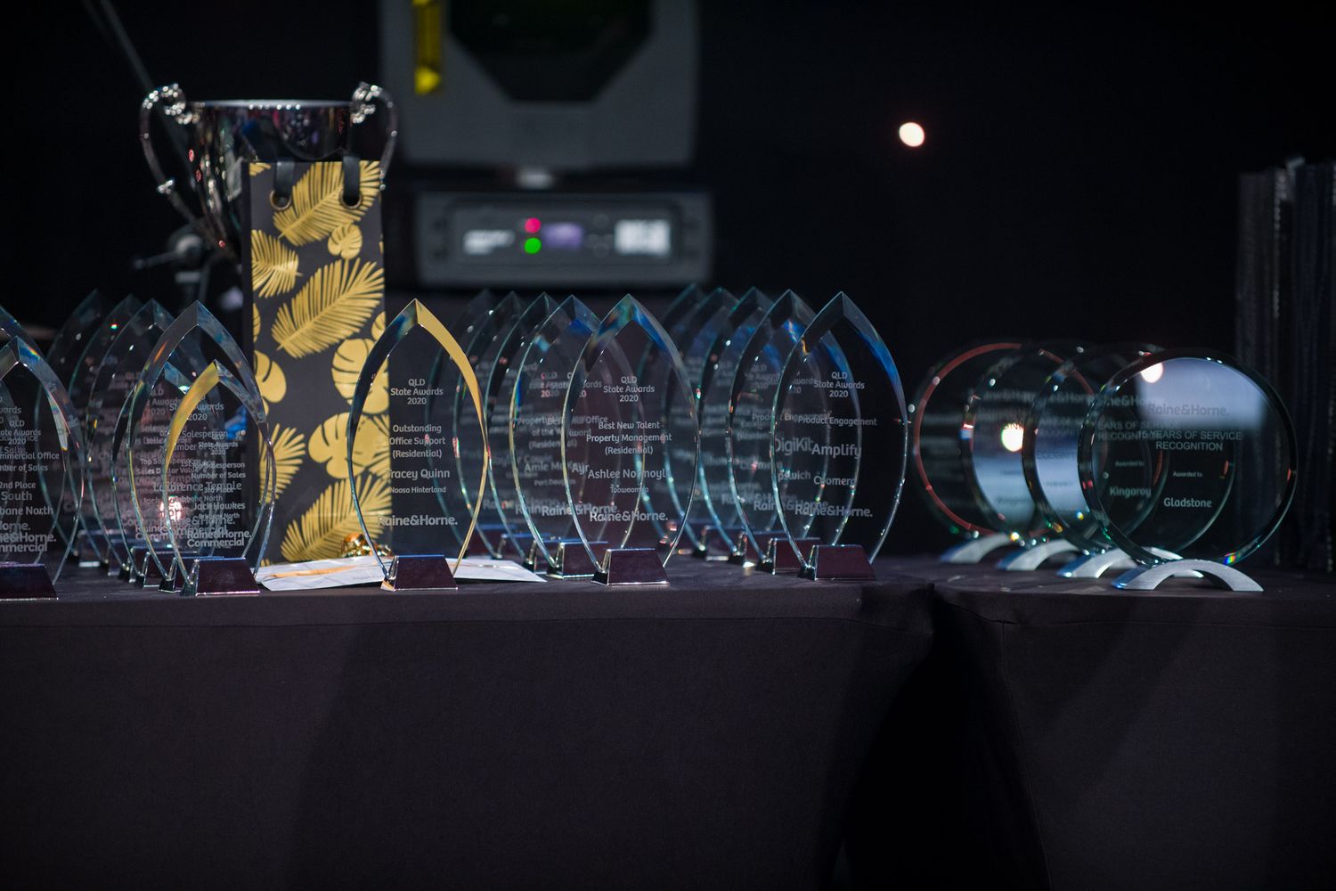 Row of glass and crystal awards trophies displayed on a draped table at a formal awards ceremony.