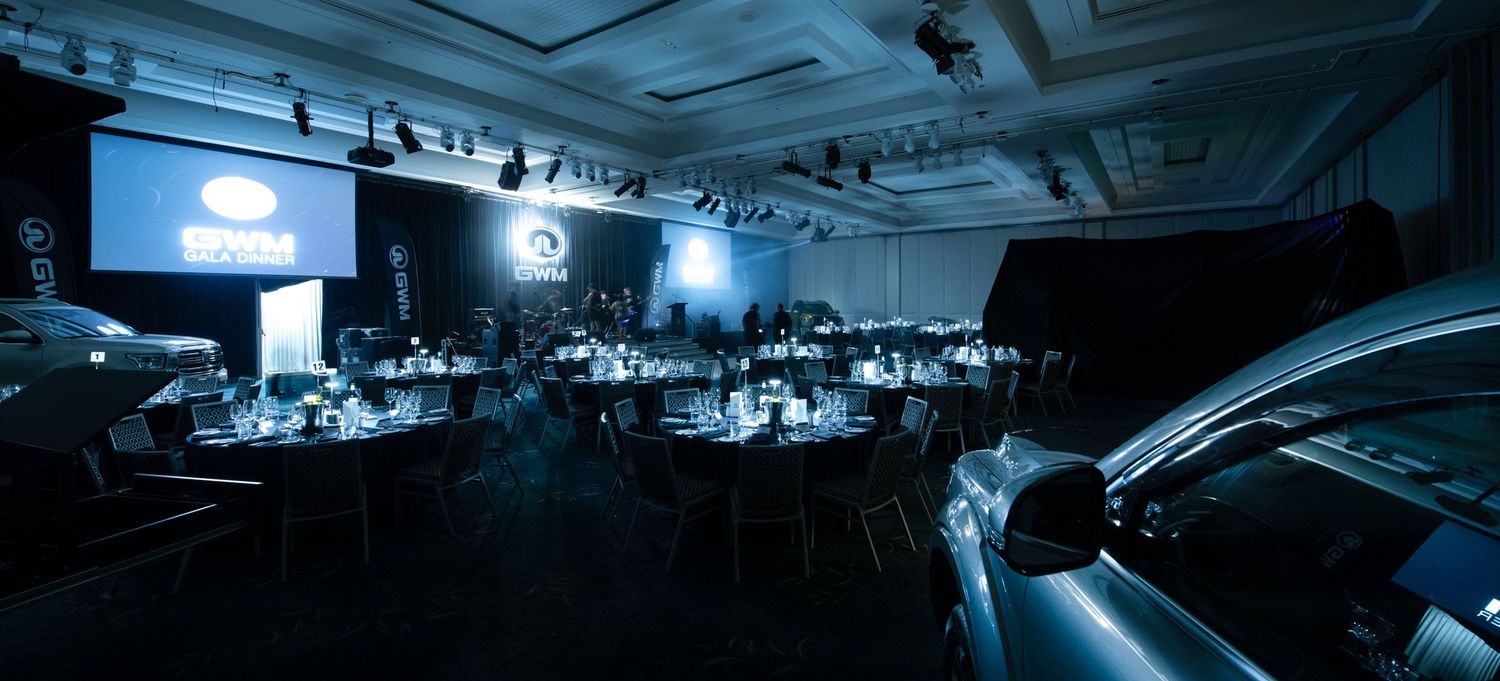 Sophisticated corporate dinner venue featuring luxury car display and branded projection screen.