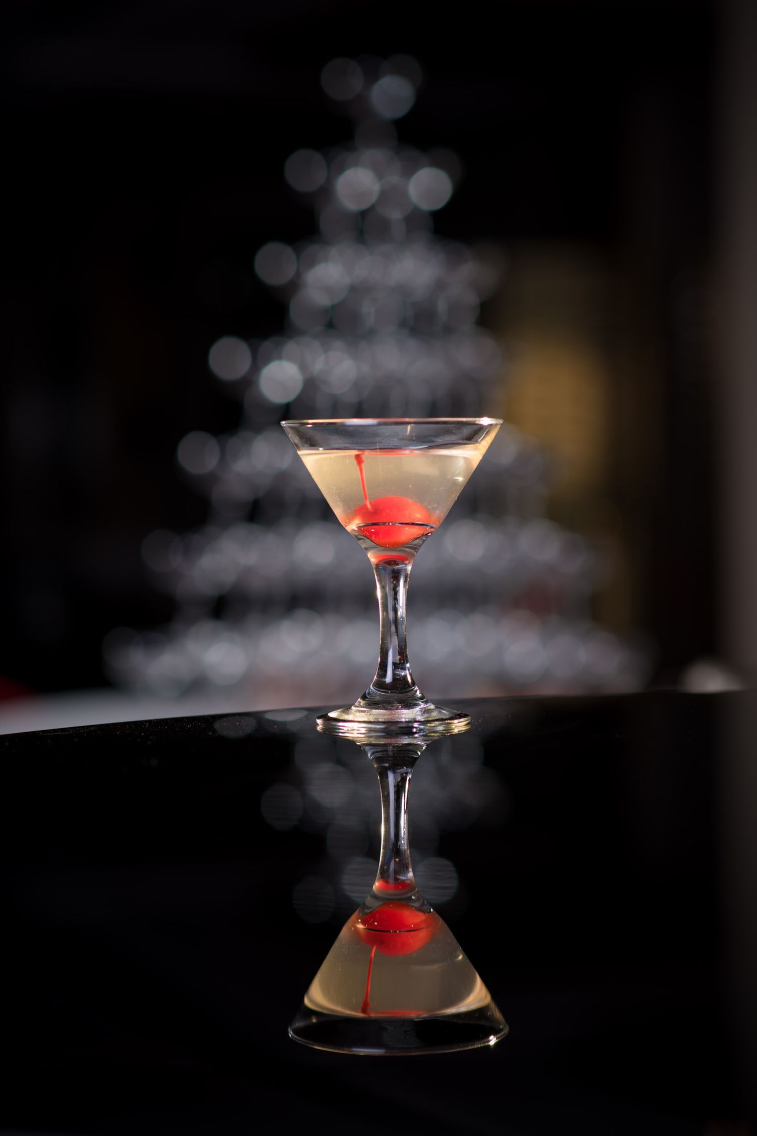 Classic martini with a red cherry garnish reflecting on a dark glossy surface.