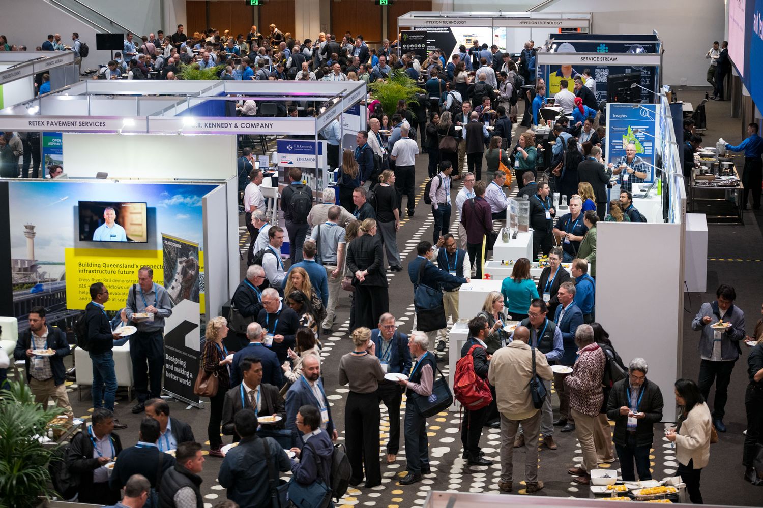 Busy trade show exhibition hall with crowds of professionals networking among vendor booths.