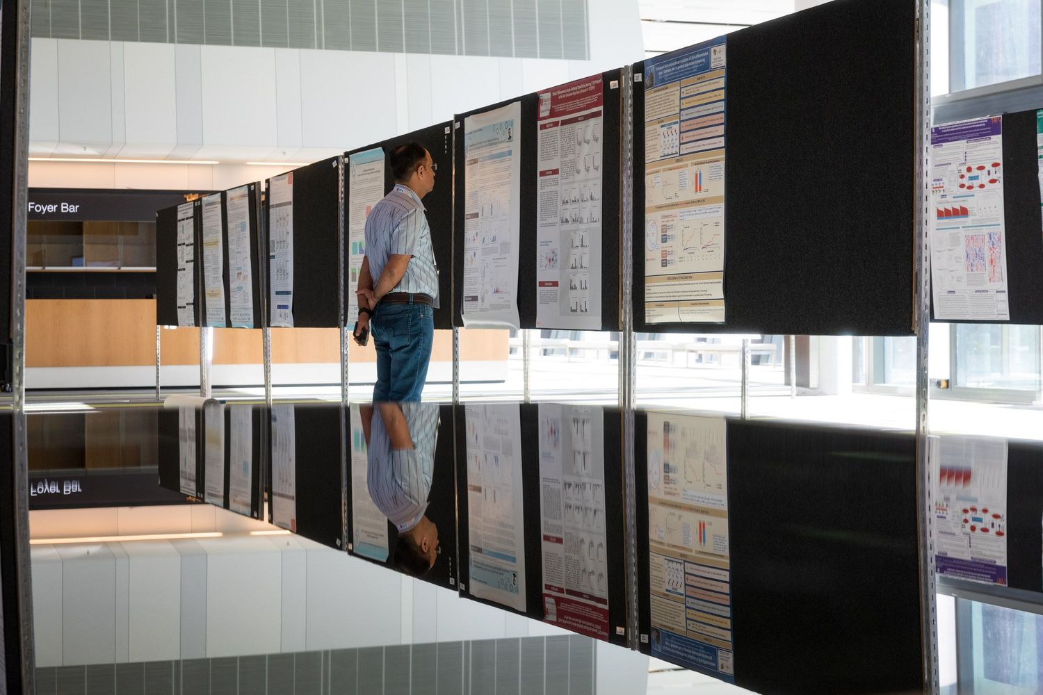 Person viewing academic research posters displayed on black panels at a professional conference exhibition.