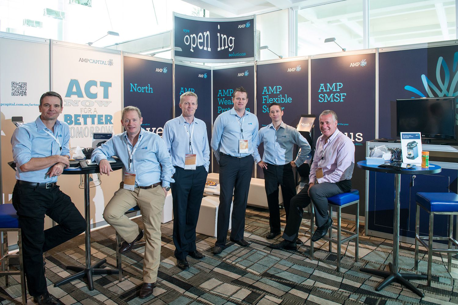 Six professionals pose together at an AMP Financial Services trade show booth at a corporate conference.