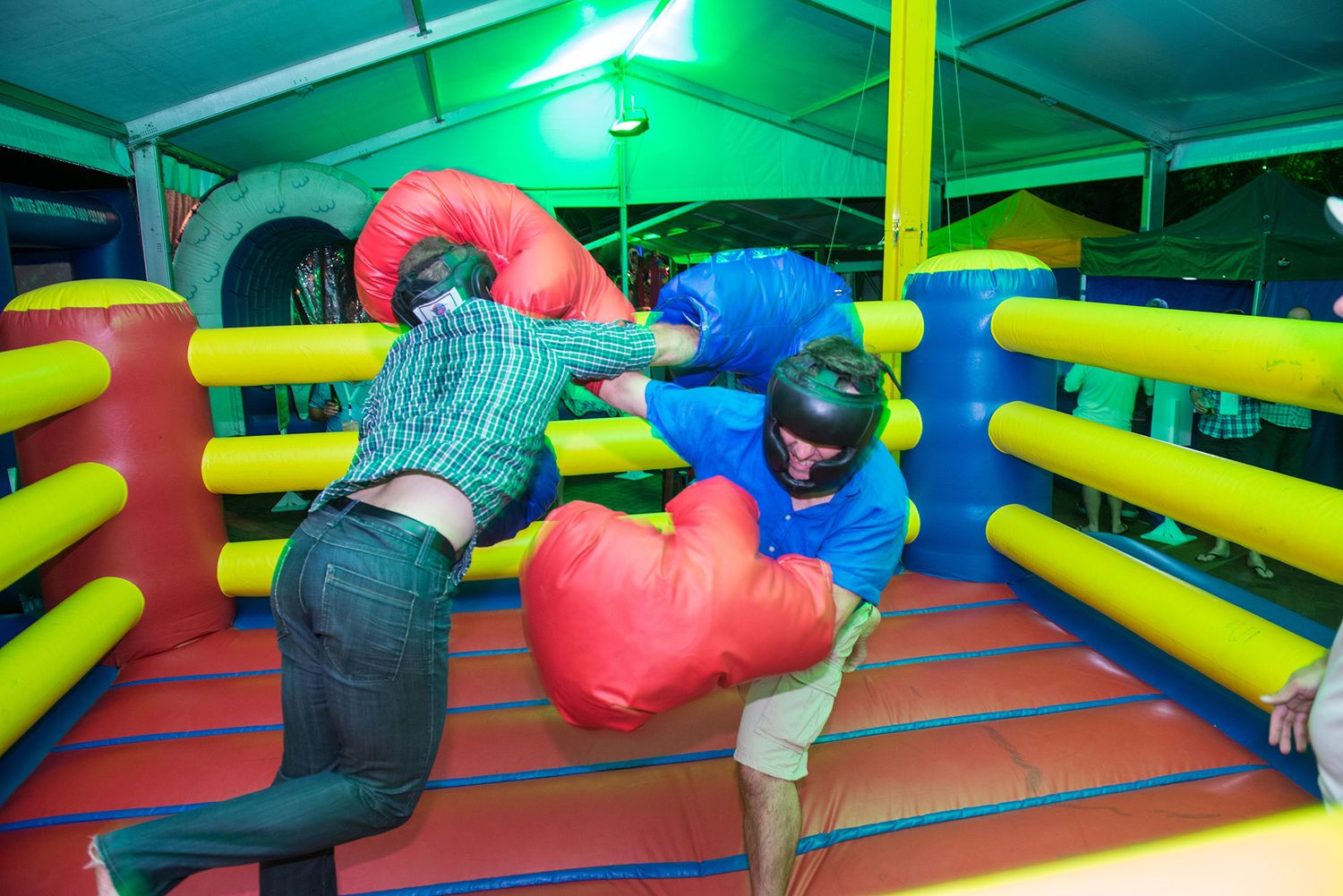Two participants wearing oversized boxing gloves compete in an inflatable boxing ring at a fun event.