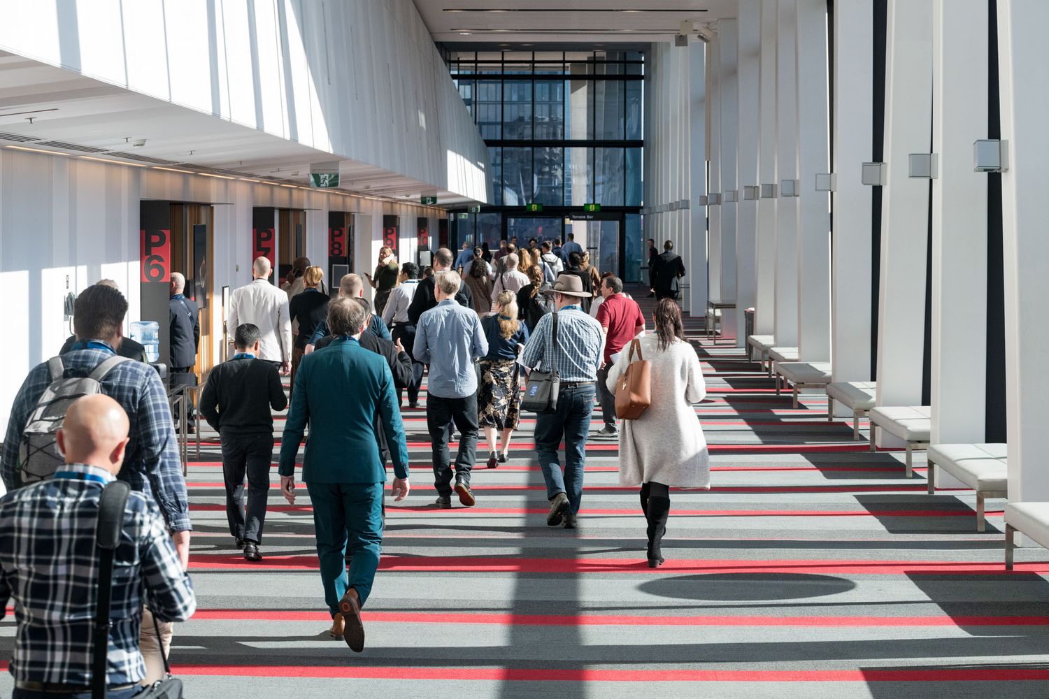Crowd of conference attendees walking through a modern venue corridor with red patterned carpet.