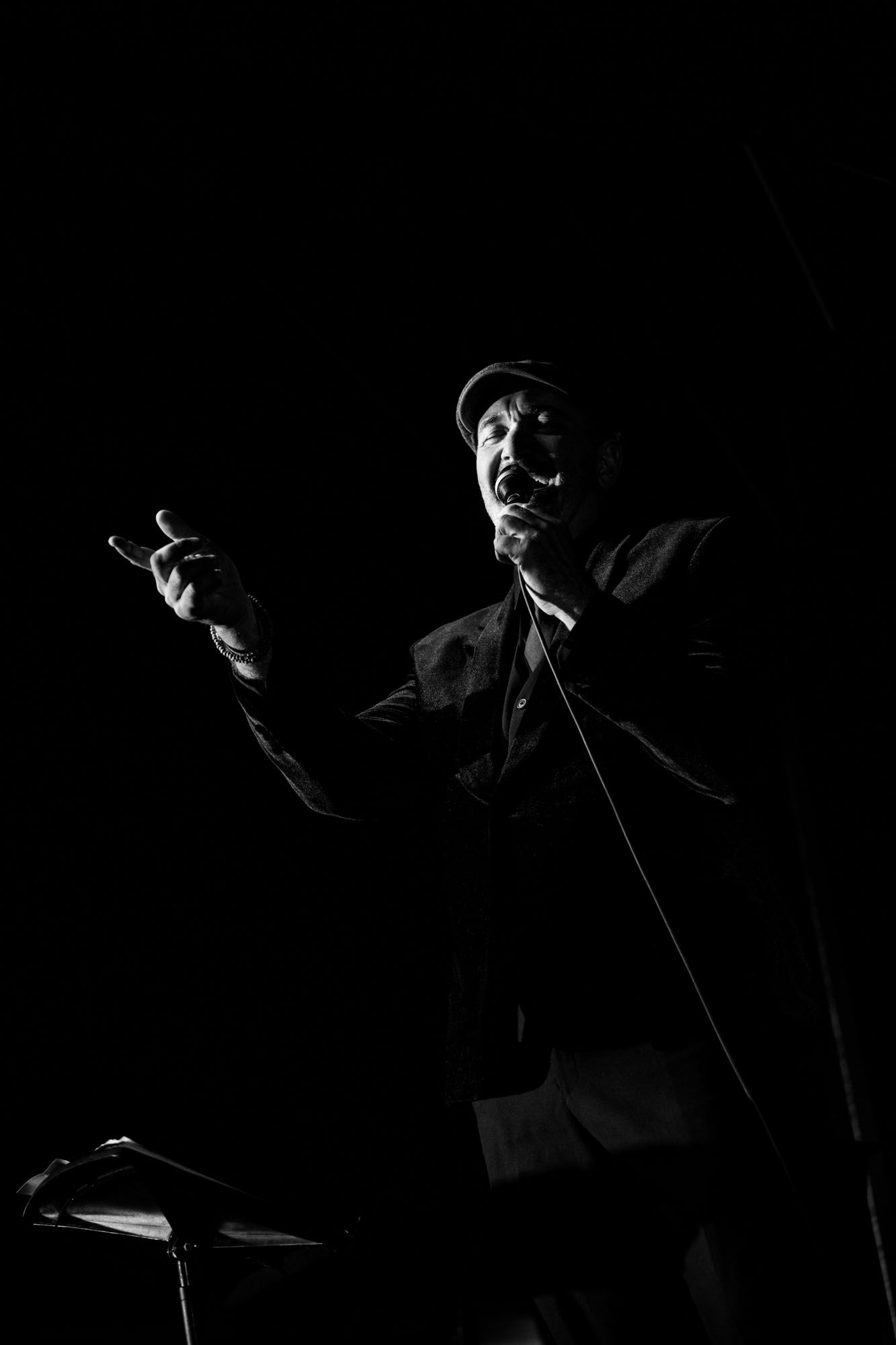 Black and white dramatic portrait of a male performer singing on stage with microphone.