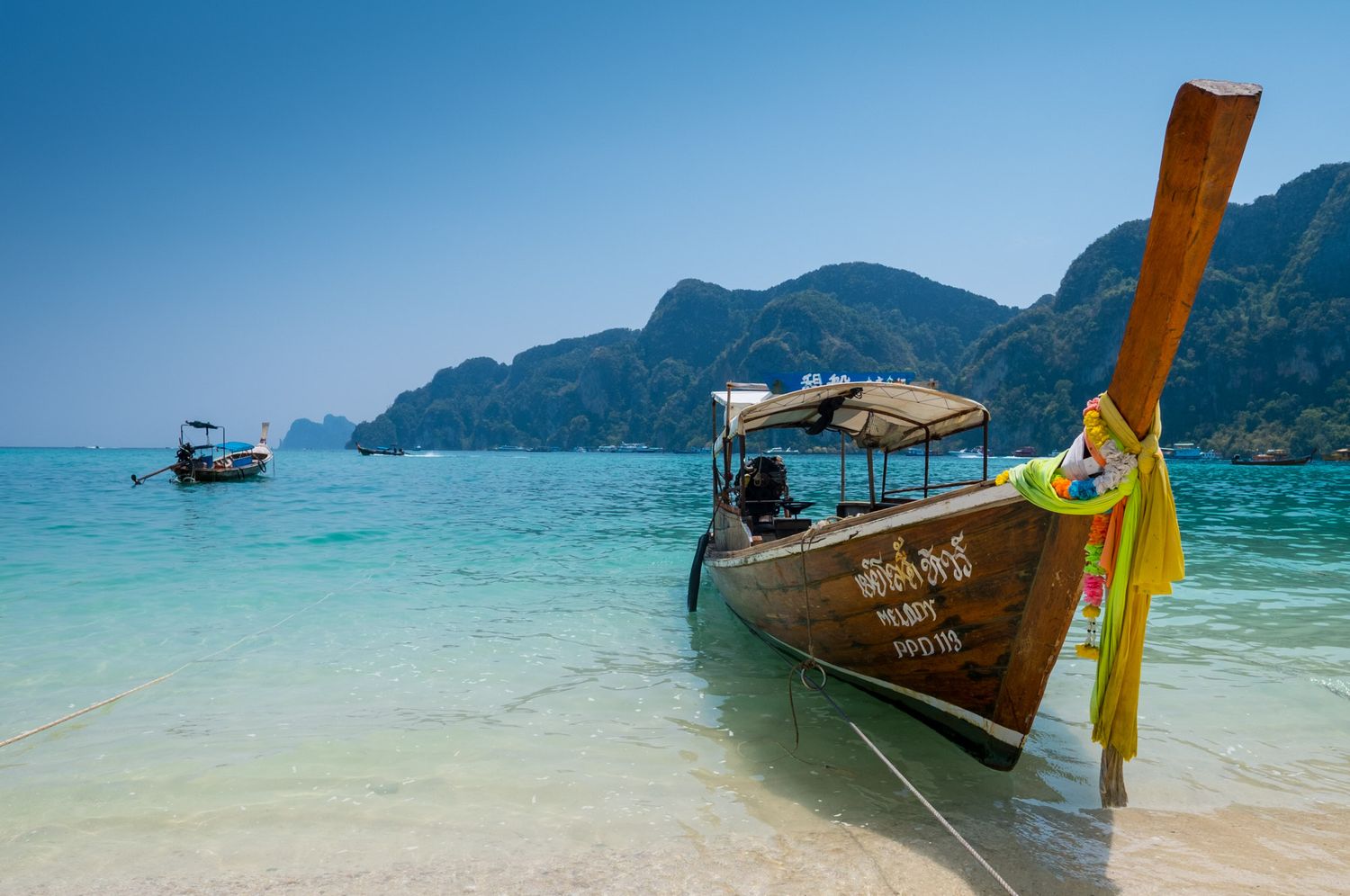 Traditional Thai longtail boat moored on a pristine turquoise beach with dramatic limestone cliffs in the background.