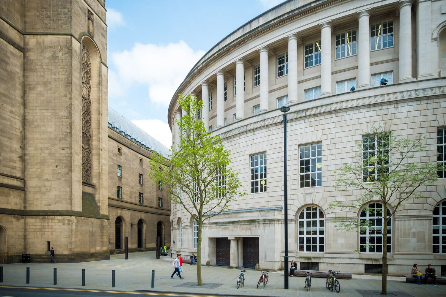 Curved neoclassical library building with tall columns and large windows on a sunny day in Manchester.