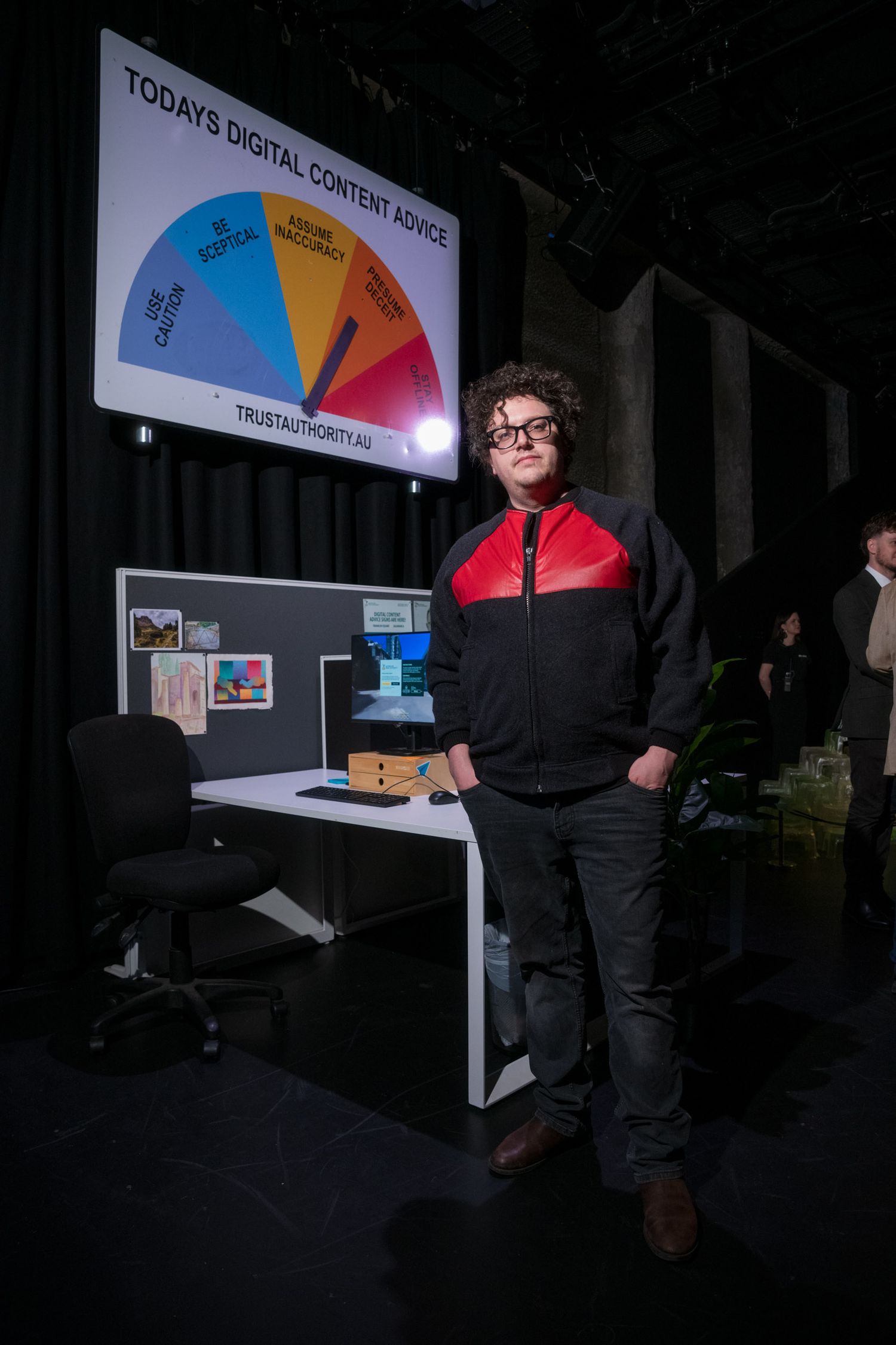 Young man in red and black jacket standing before digital content advice display board.
