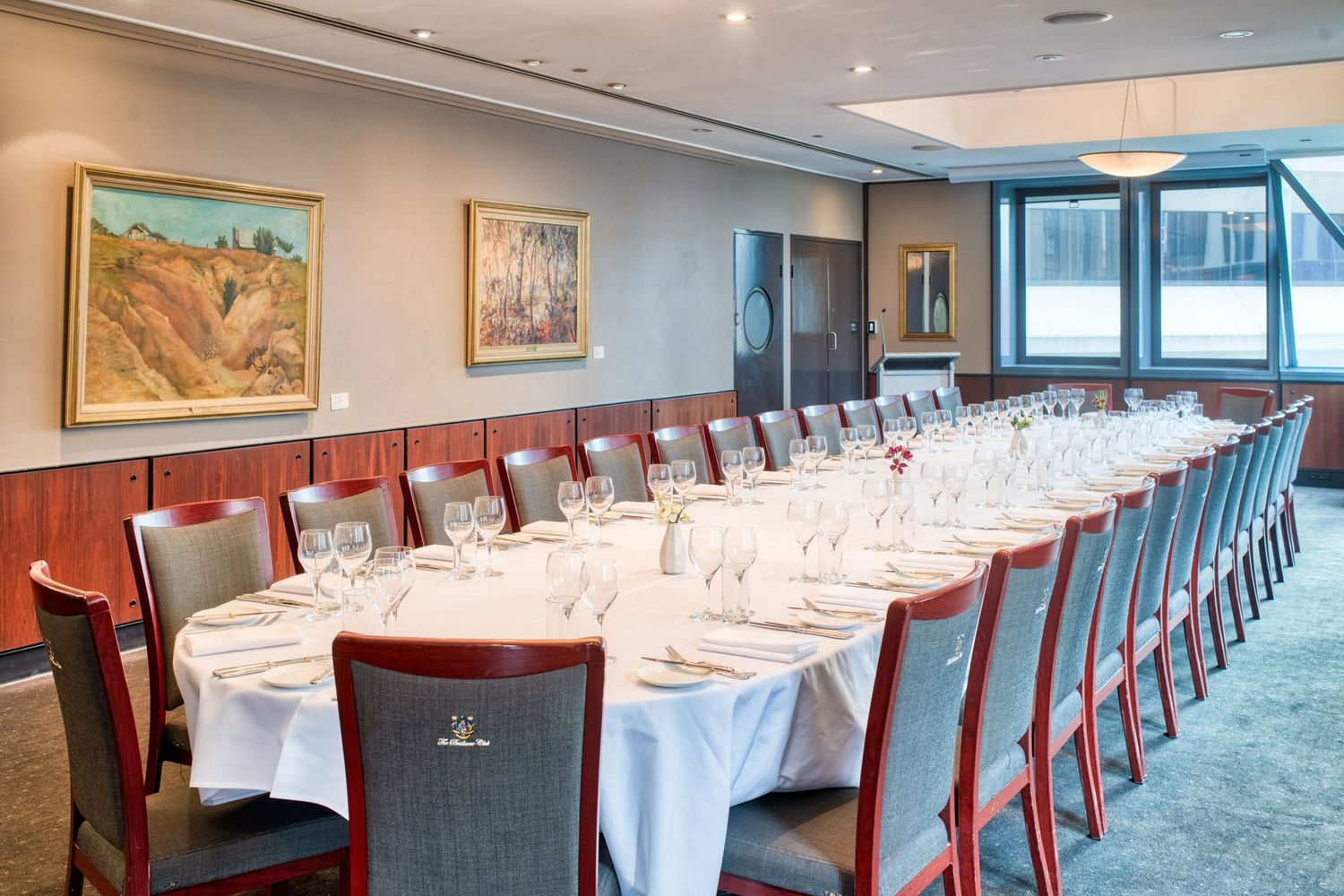 Elegant private dining room with long white-clothed table set for formal dinner with wine glasses and artwork on walls.