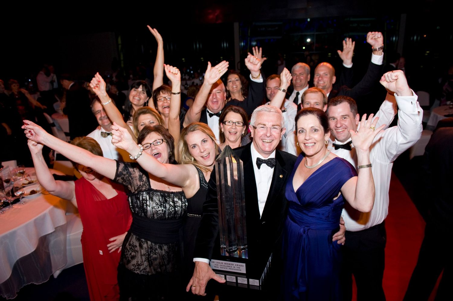 Excited crowd of formally dressed guests celebrating at a gala awards dinner event.