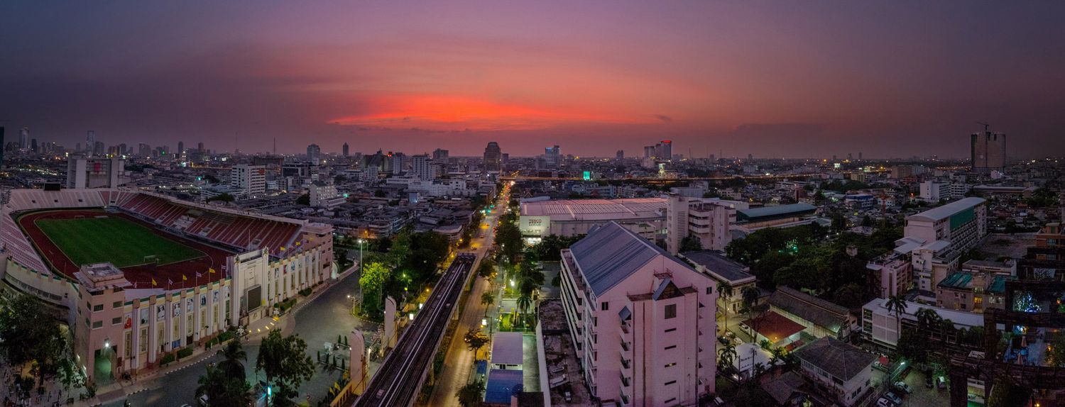 Aerial panoramic view of Bangkok city skyline illuminated at twilight with vibrant purple and orange sky.