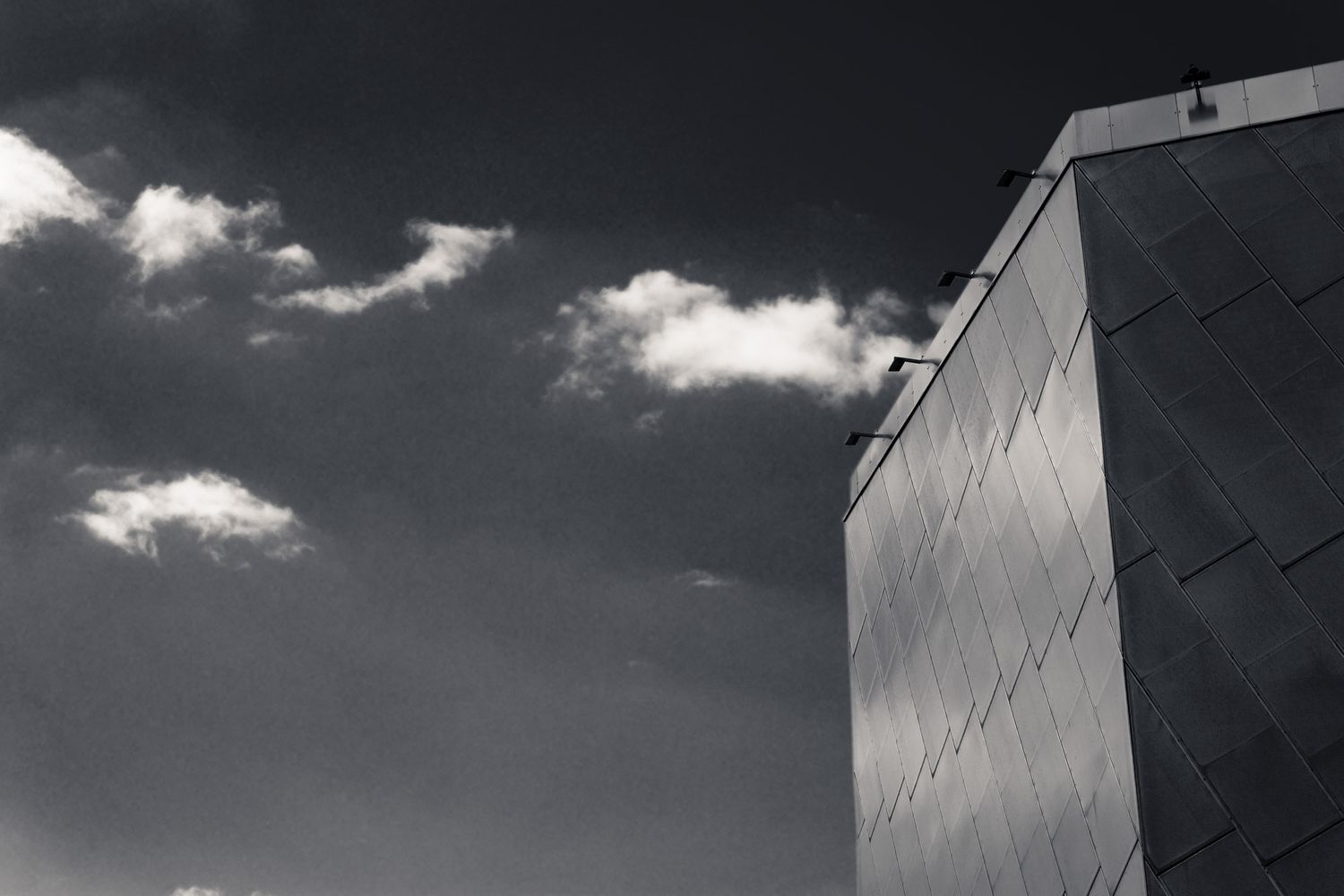 Black and white photo of a modern angular building facade against a dramatic cloudy sky.