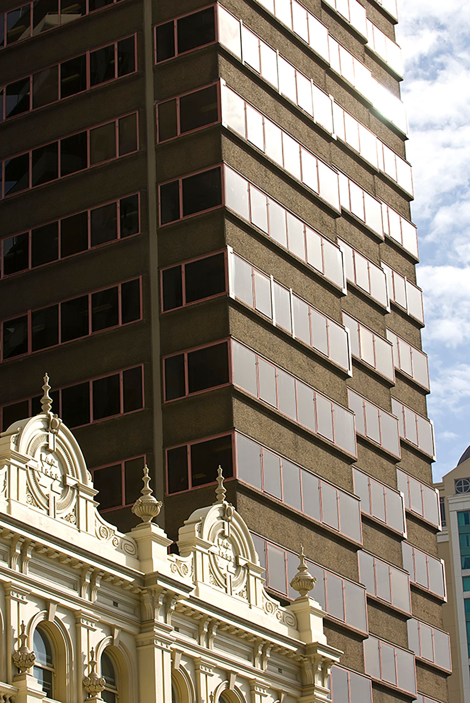 Contrast of ornate heritage building facade against modern glass and brown office tower in city center.