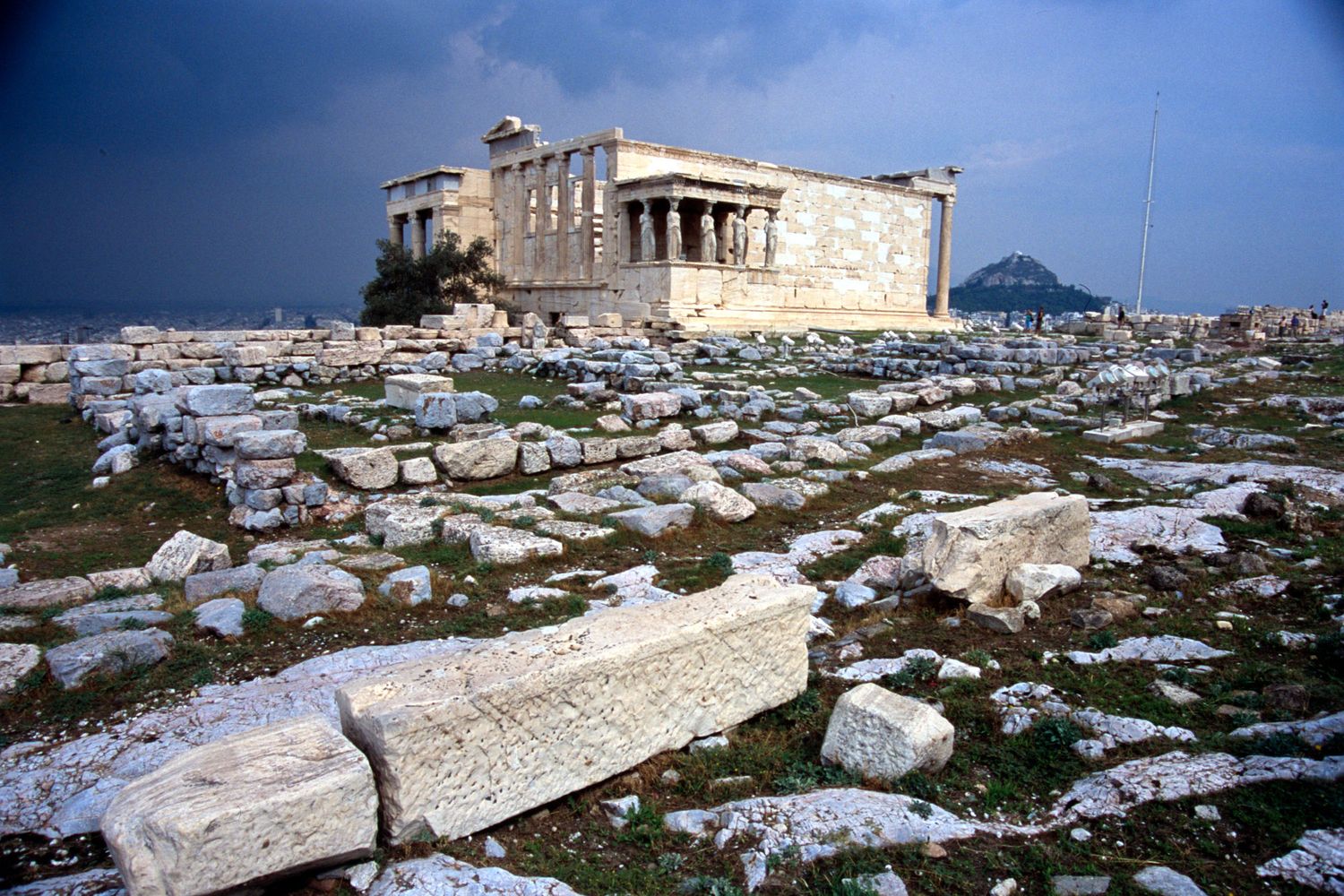 Ancient Greek Erechtheion temple ruins on the Acropolis of Athens with scattered marble fragments.