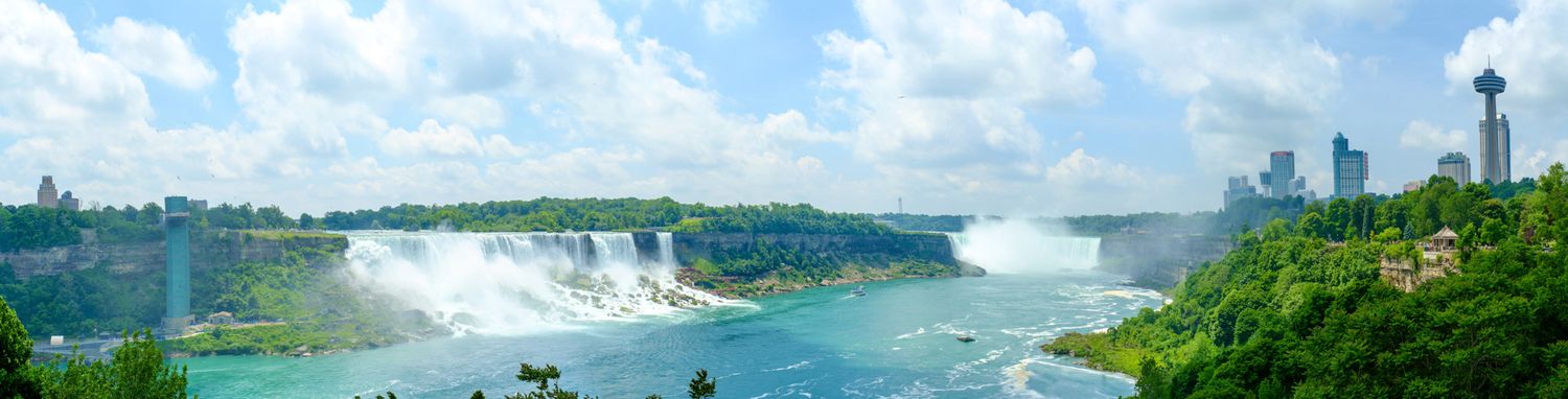 Panoramic view of majestic Niagara Falls with mist rising and observation towers visible in the distance.