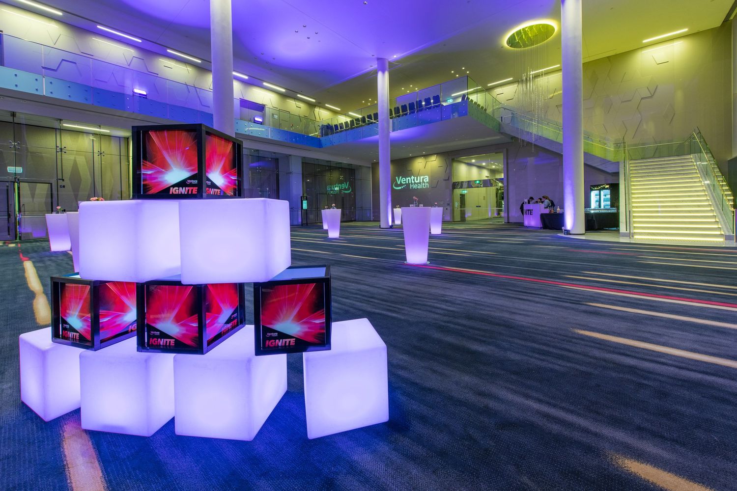Modern event venue foyer with illuminated white cube displays featuring colorful graphics and glowing tall vases.
