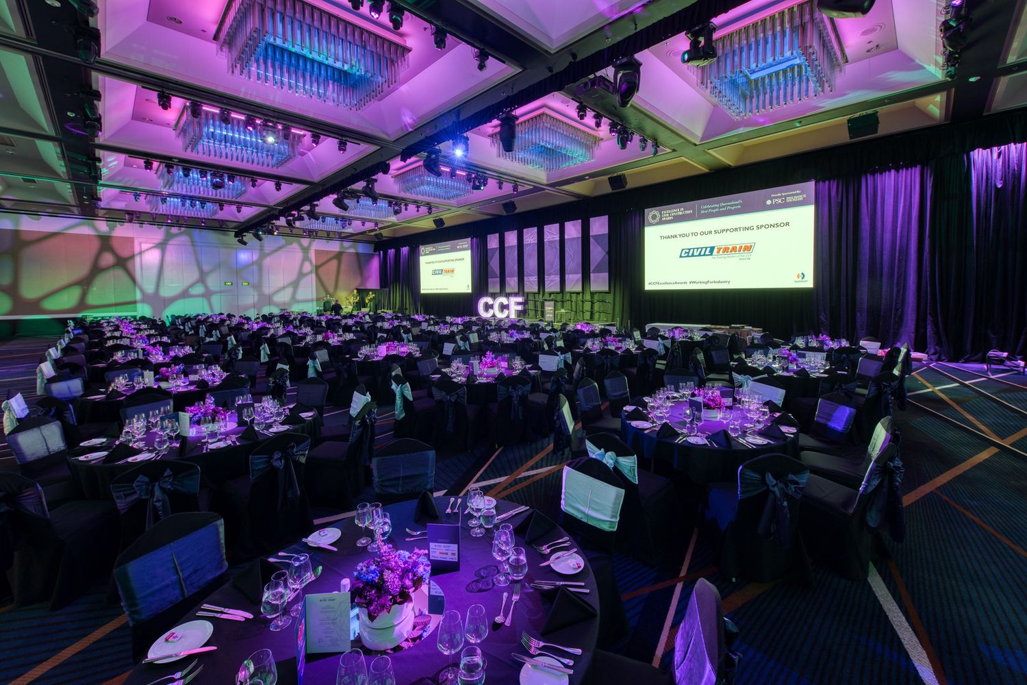 Large CCF awards dinner banquet hall with round tables and colorful stage lighting.
