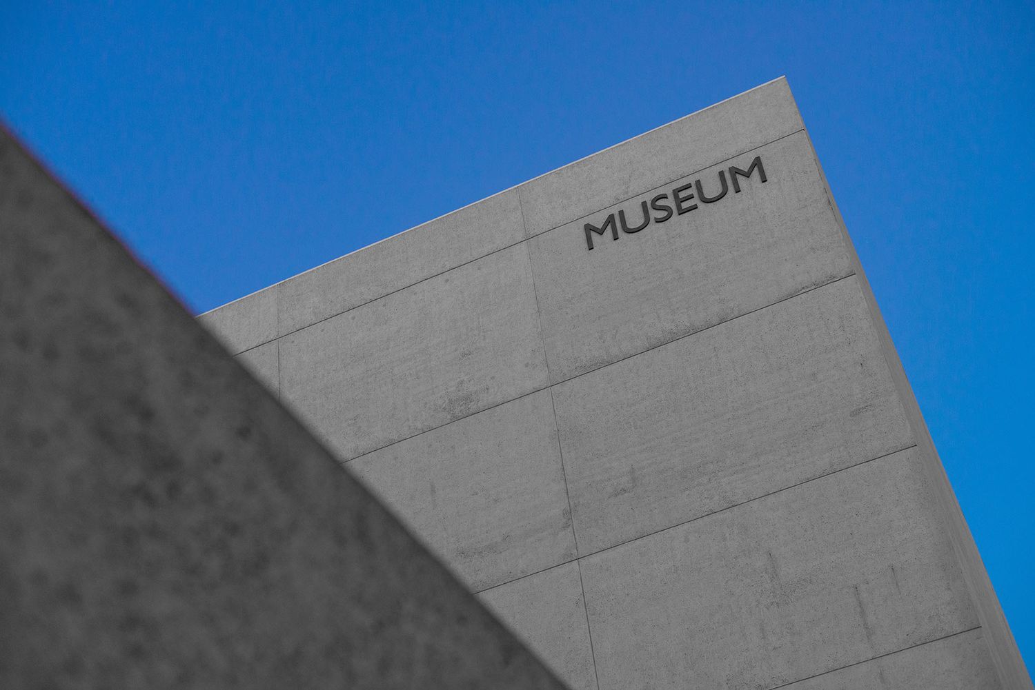 Modern concrete museum building exterior with bold MUSEUM text against a clear blue sky.