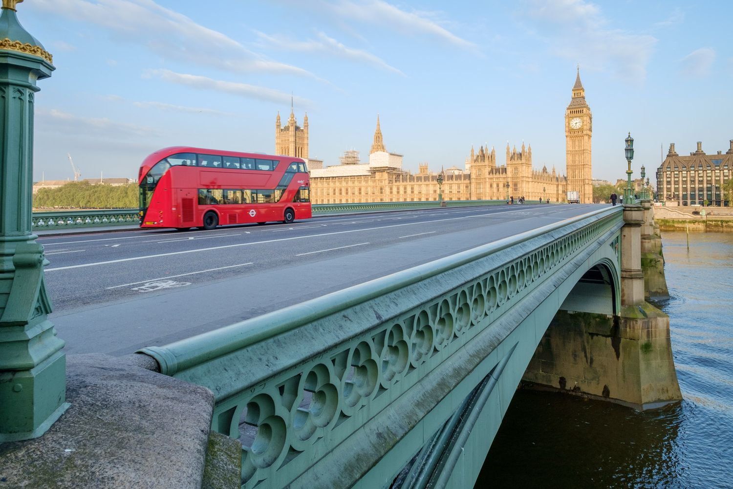 Iconic red double-decker bus crossing Westminster Bridge with Big Ben and Parliament in London at sunrise.