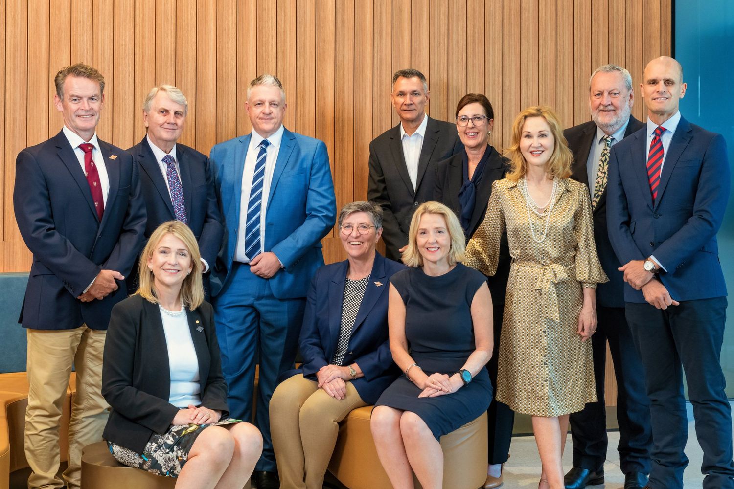 Group of eleven business professionals posing for a formal team photo in a modern office setting.