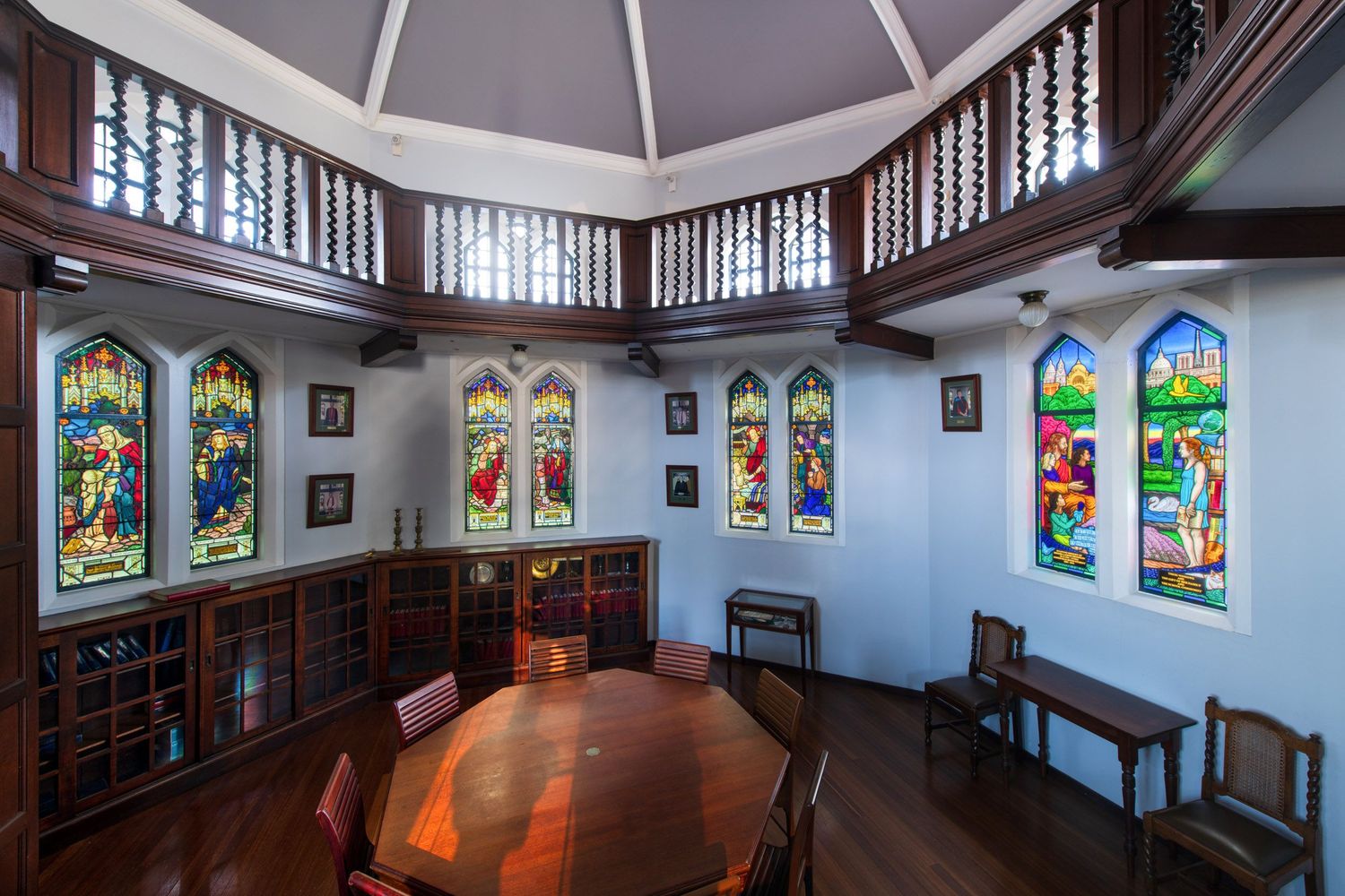 Elegant dining room with stained glass windows, wooden balcony, and oval table in a historic octagonal building.