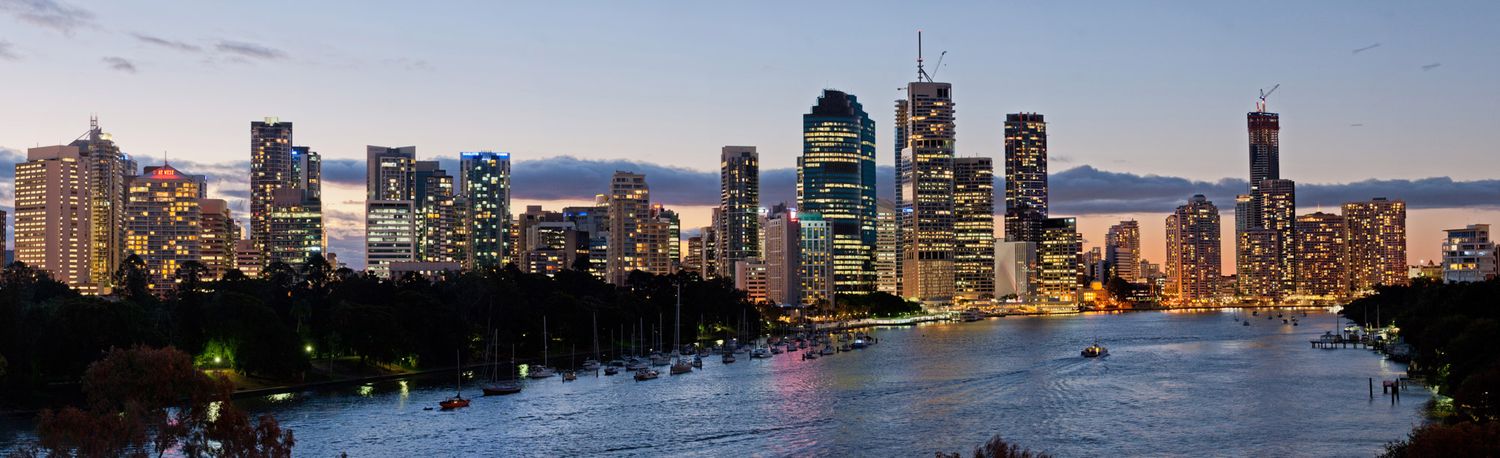 Brisbane city skyline panorama at dusk with river reflections and illuminated skyscrapers.
