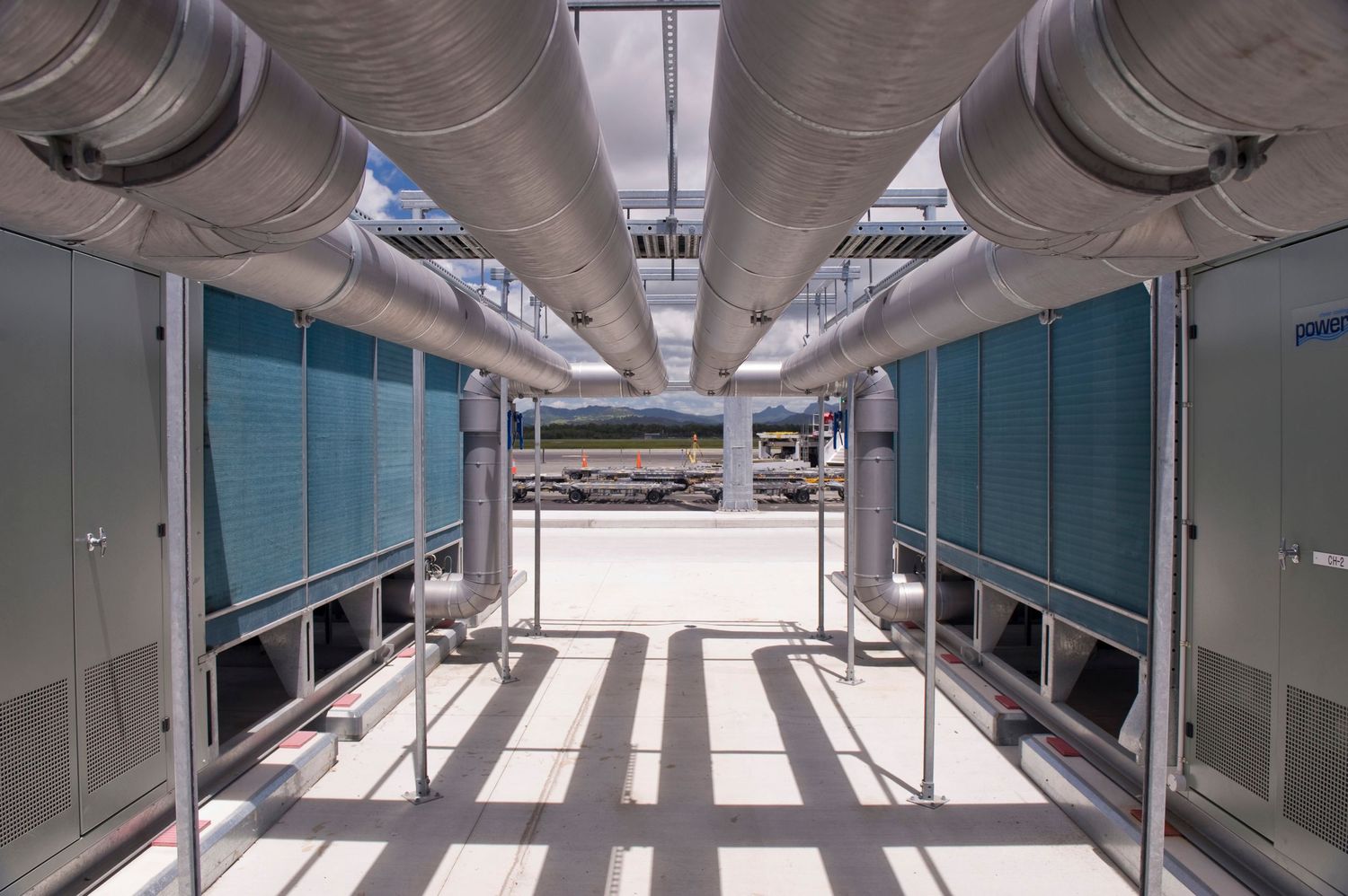 Modern data center corridor with large silver ventilation ducts and teal server units.