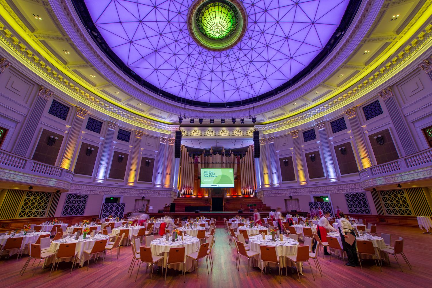 Grand circular ballroom with ornate domed ceiling, purple lighting, and round tables set for a formal gala.
