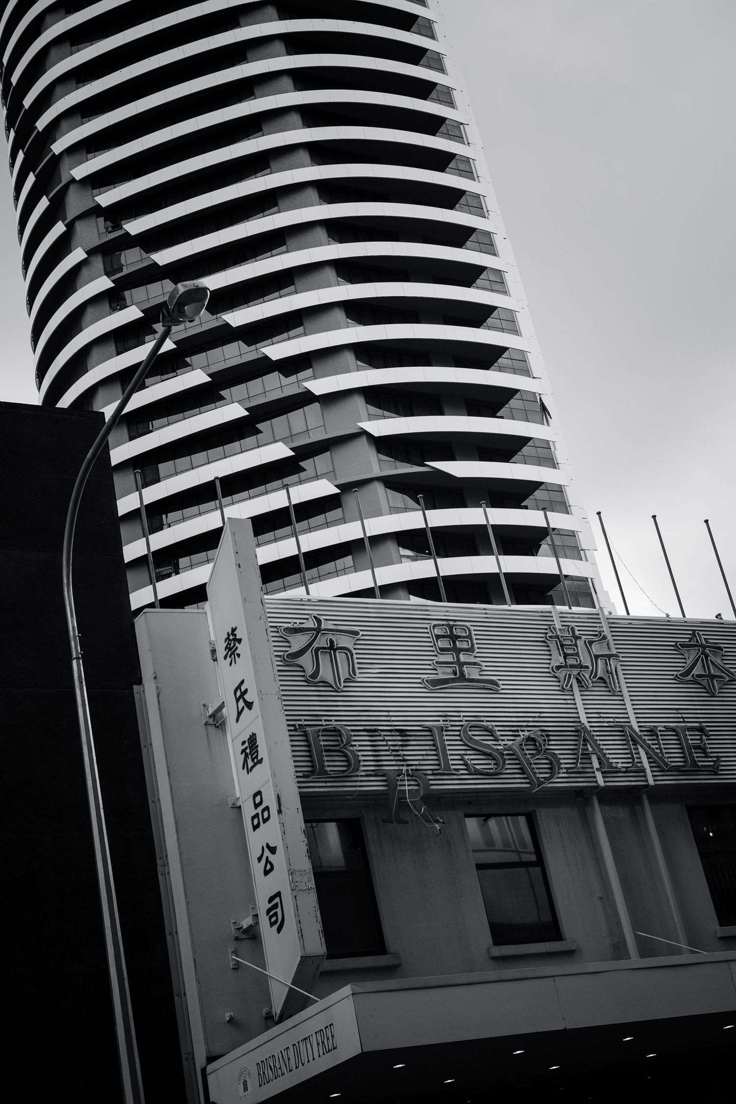 Black and white photo of Brisbane city buildings with Chinese signage and curved modern skyscraper.