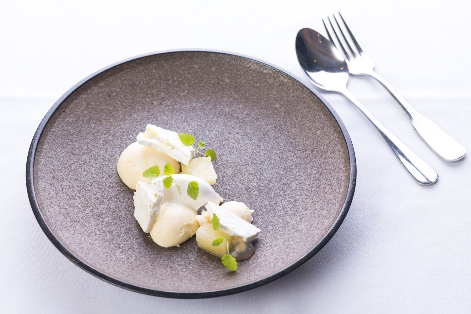 Elegant fine dining dessert with white cream and microgreens on a gray plate.