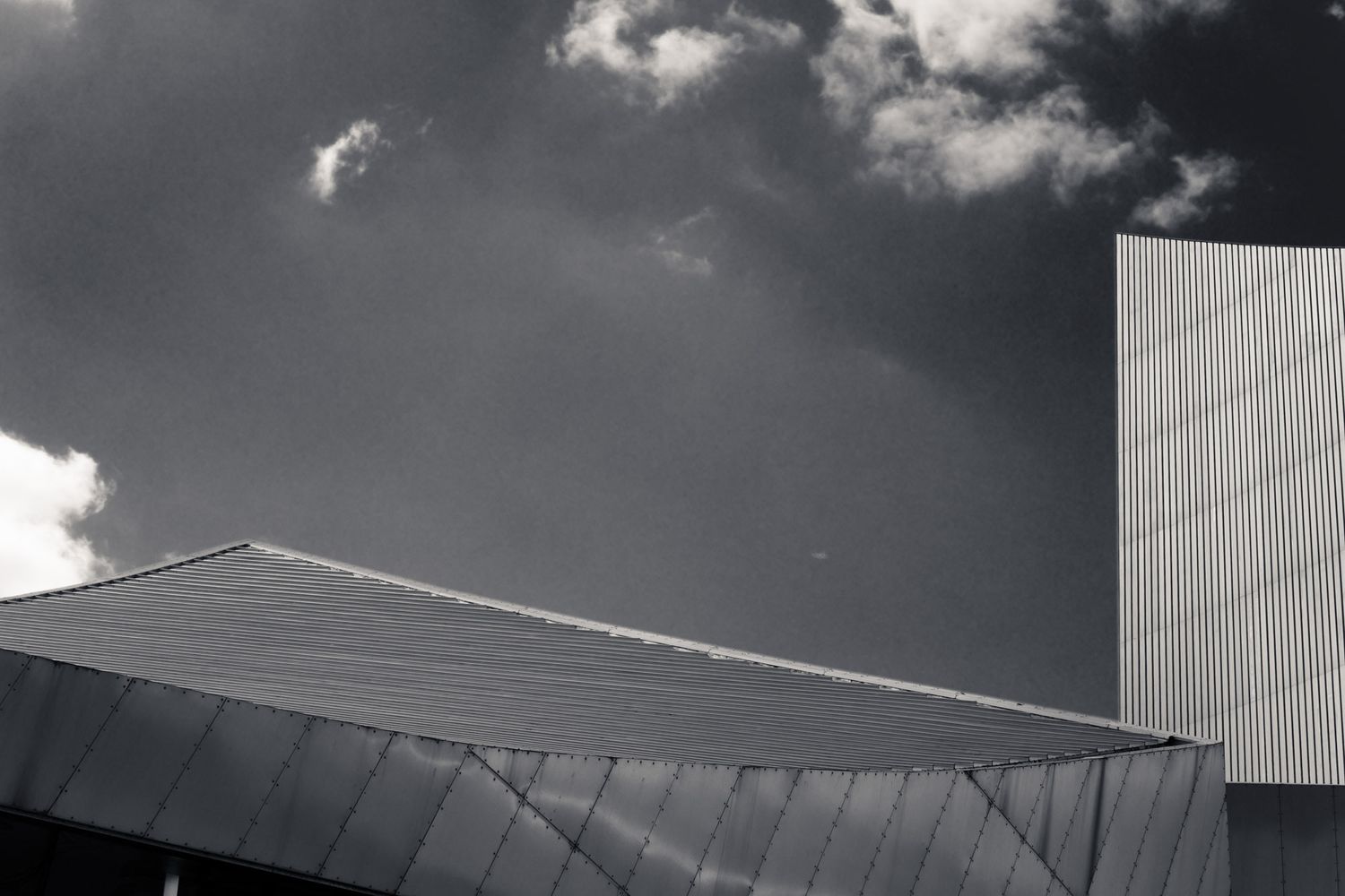 Black and white photo of a modern metallic building rooftop against a dramatic stormy sky.