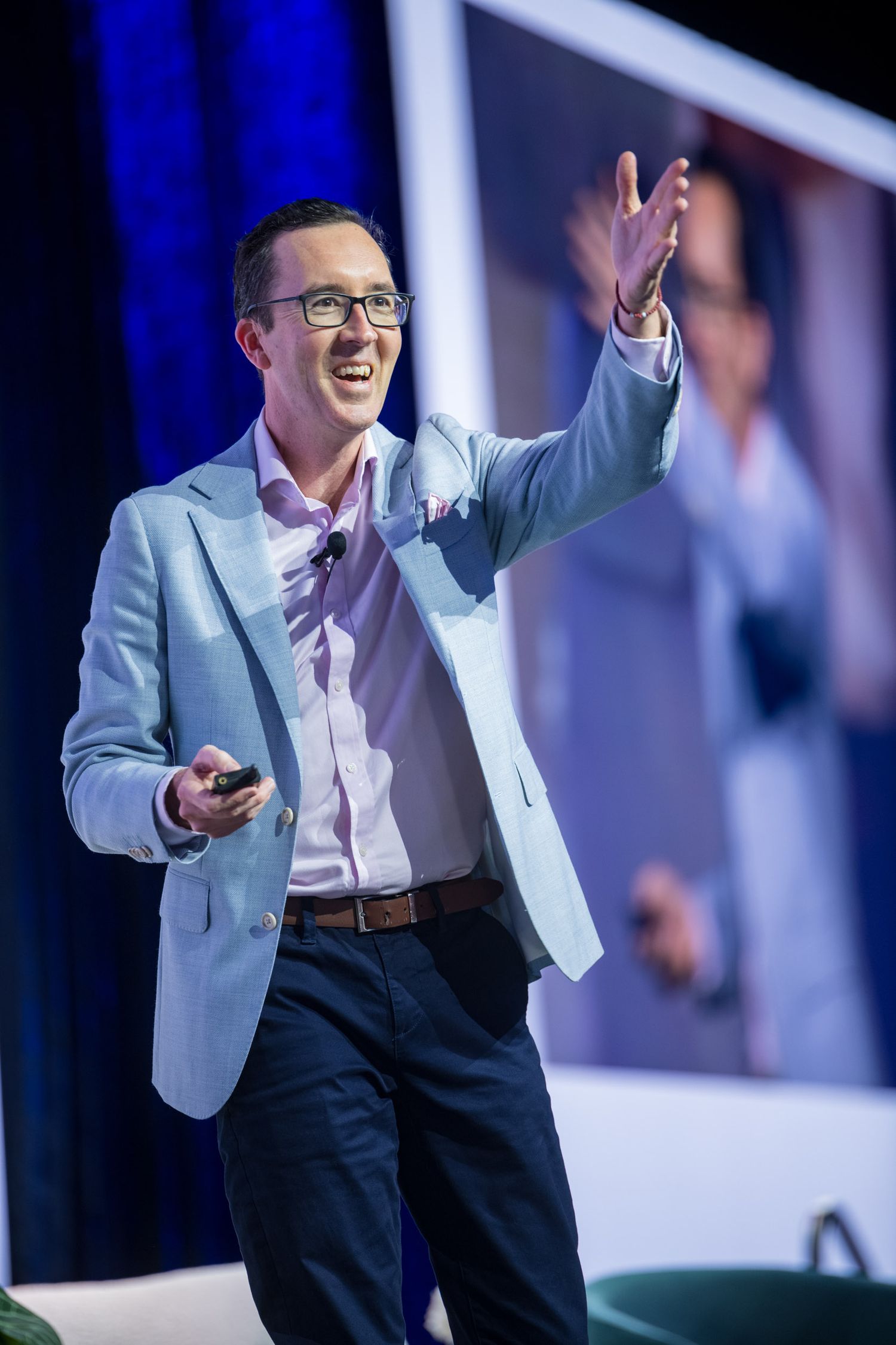 Enthusiastic male speaker in light blue blazer gestures with raised arm at business conference.