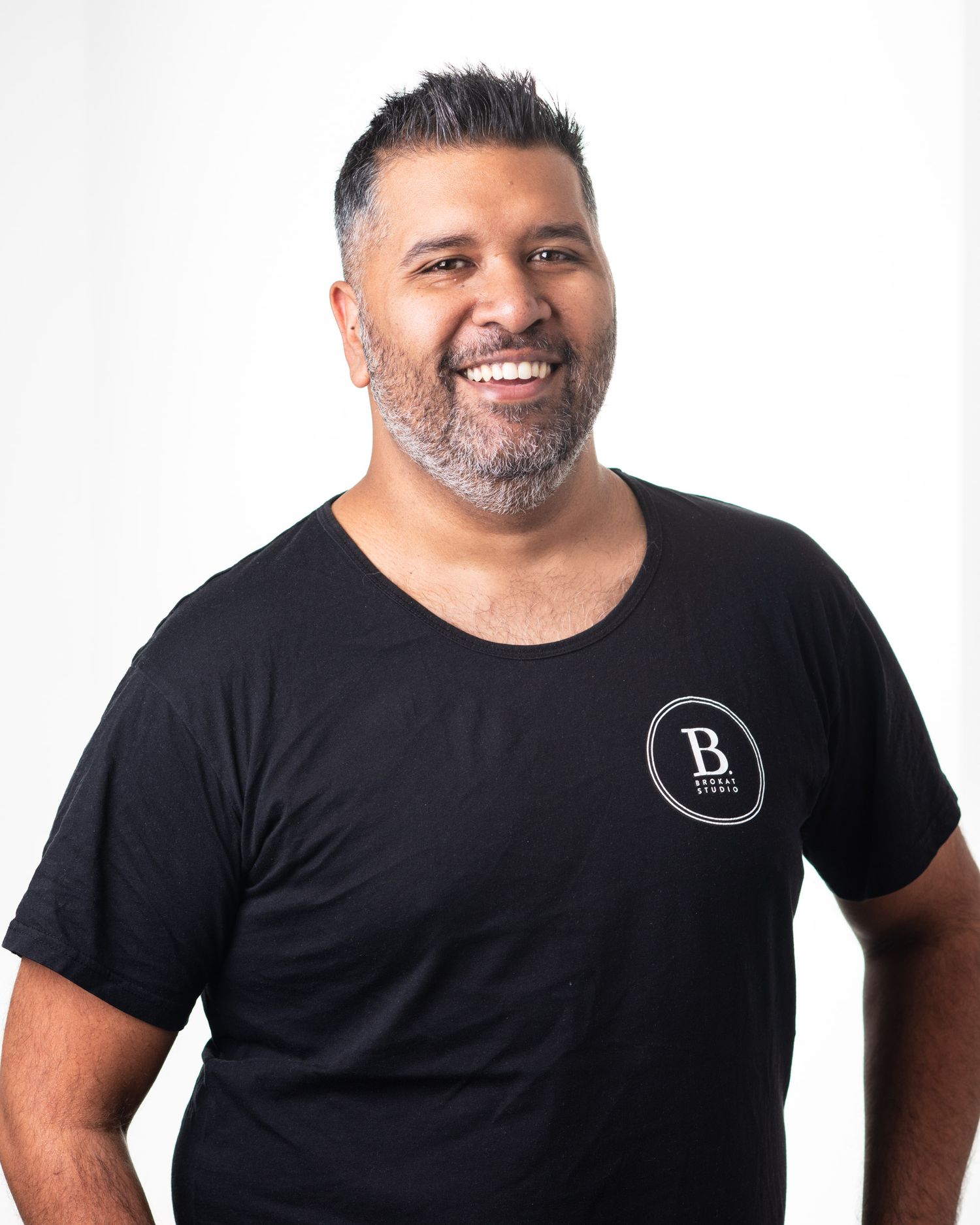 Smiling man with beard wearing a black branded t-shirt against a clean white studio background.