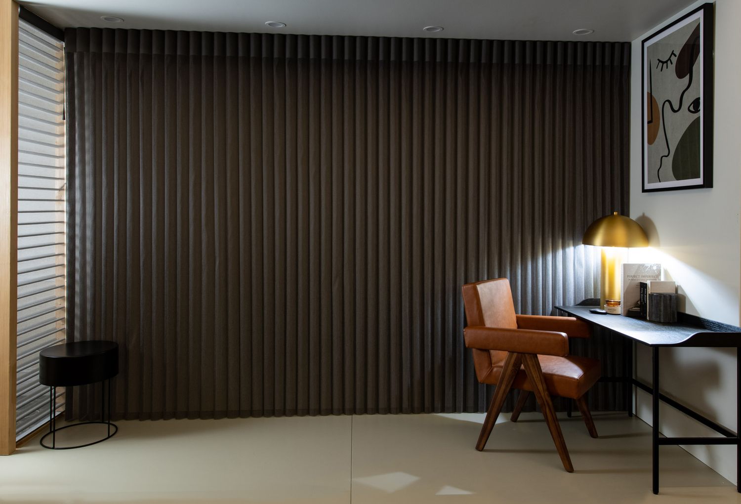 Contemporary home office with dark vertical wall panels, a wooden desk, gold lamp, and modern chair at dusk.