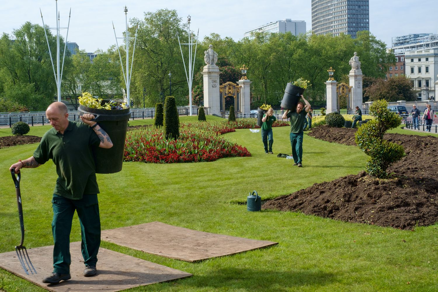 Gardeners maintaining colorful flower beds in a formal London park near a white gate.