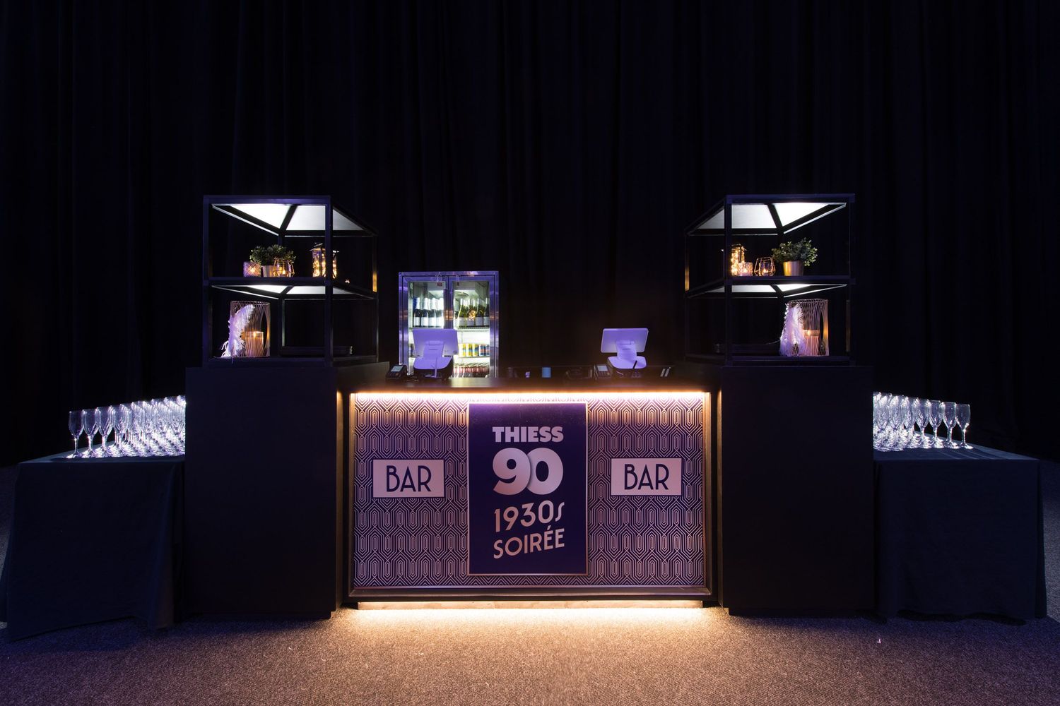 Elegant Thiess 90th anniversary 1930s soiree bar setup with illuminated display and glassware.