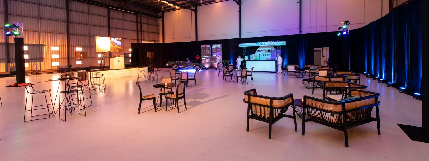 Spacious industrial event venue with mixed seating, warm lighting, and a stage backdrop for a corporate function.