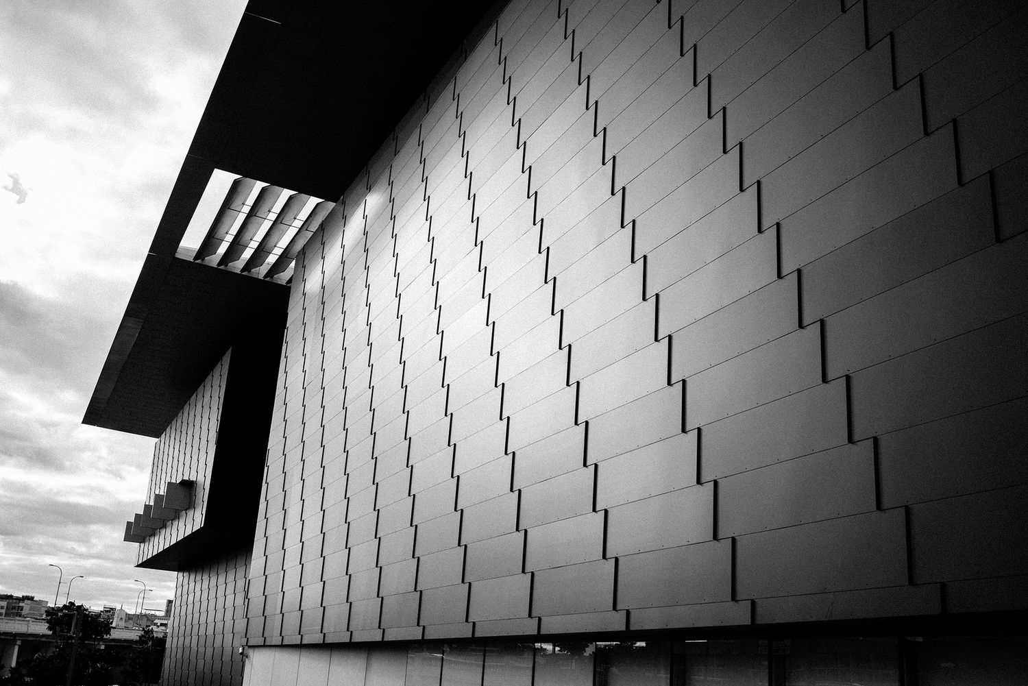 Black and white architectural shot of modern building exterior with geometric patterned metal cladding panels.