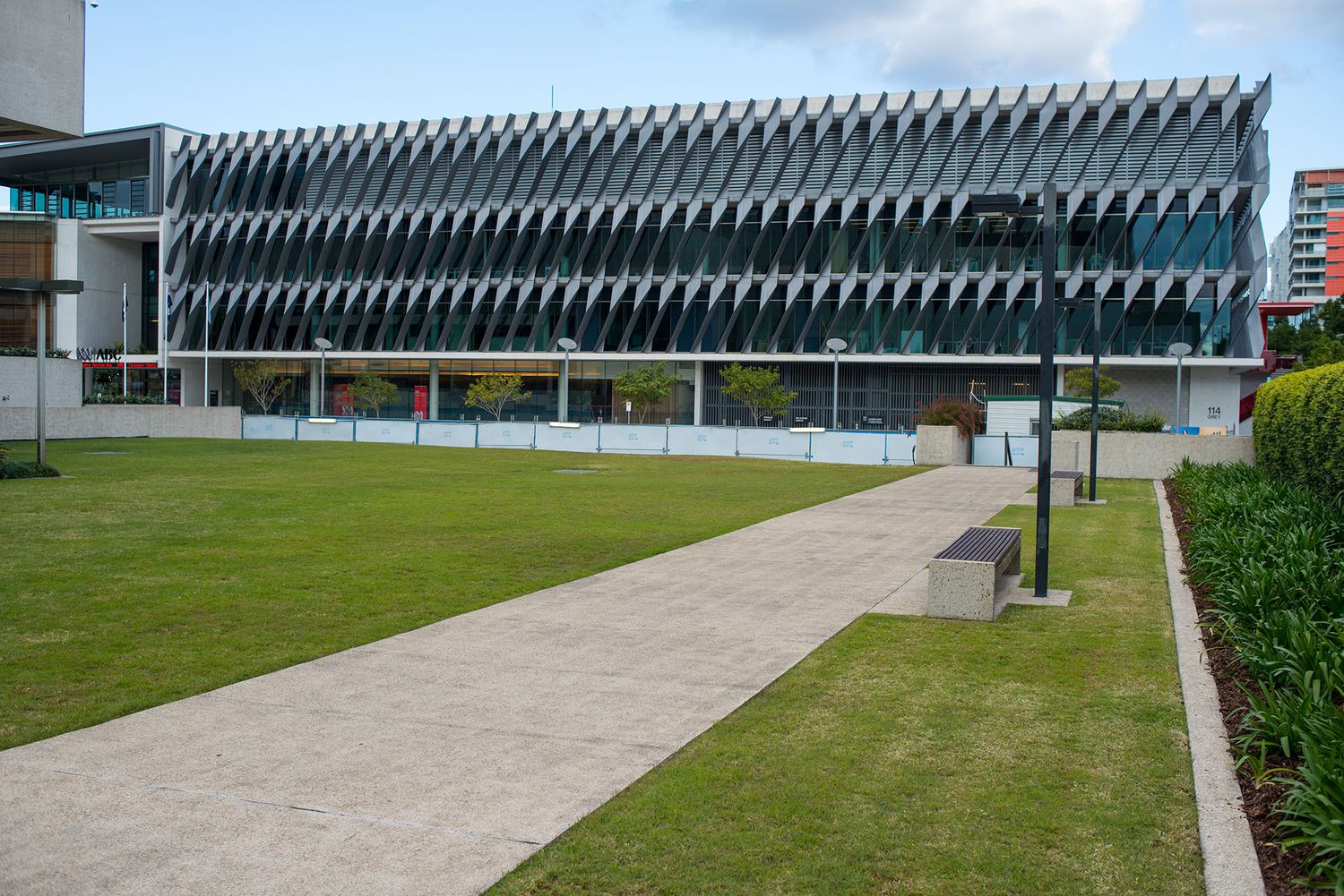 Modern building with striking angular facade and green lawn pathway under partly cloudy sky.