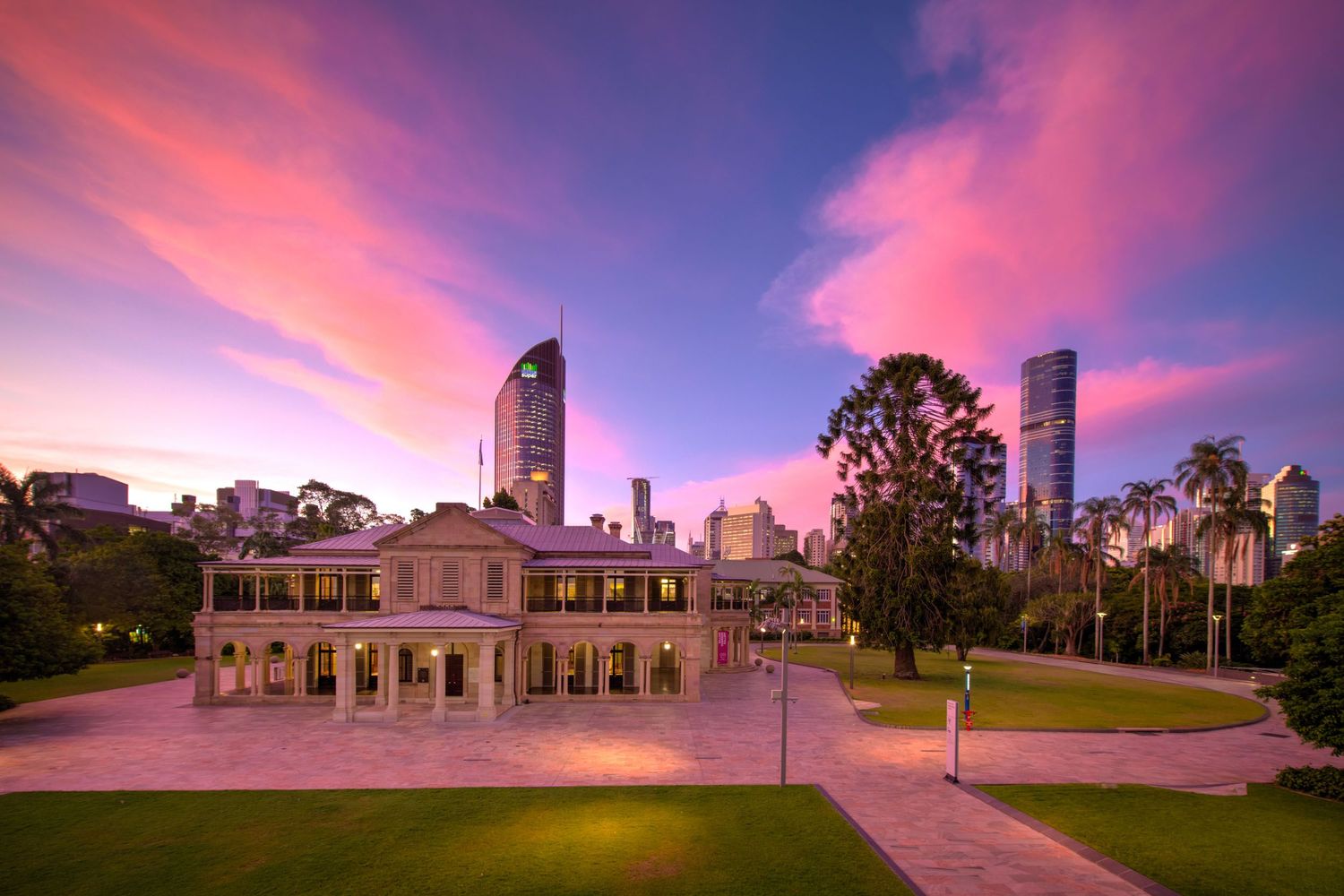 Historic Queensland government building at sunset with vibrant pink sky and city skyline.