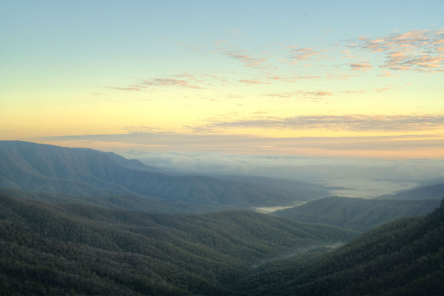 Aerial sunrise view over lush green mountain valleys with golden sky and misty horizon.