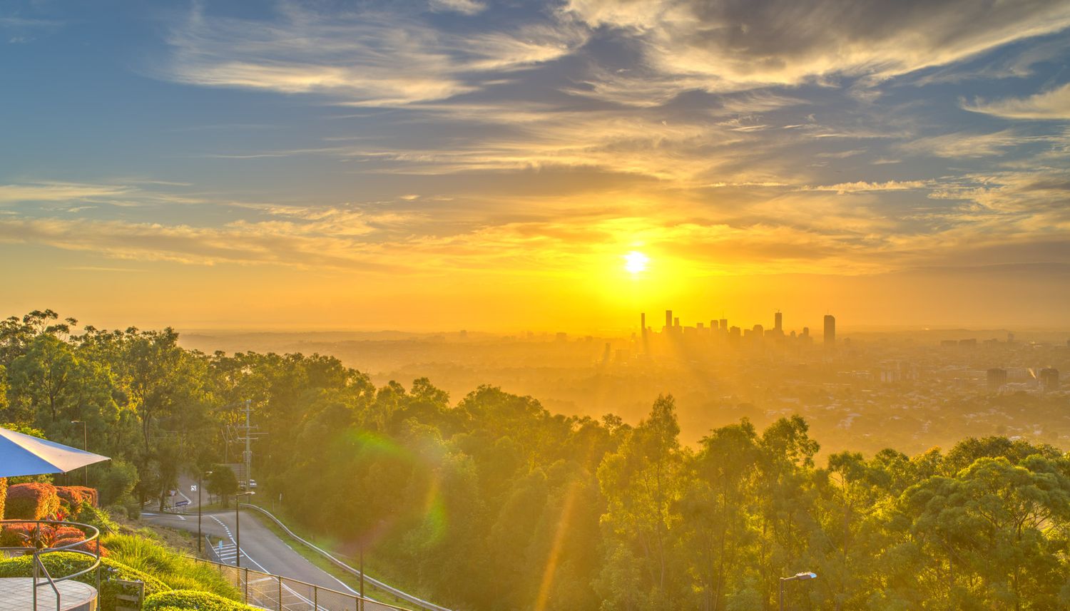 Golden sunrise over a lush city skyline with trees and roads bathed in warm orange light.