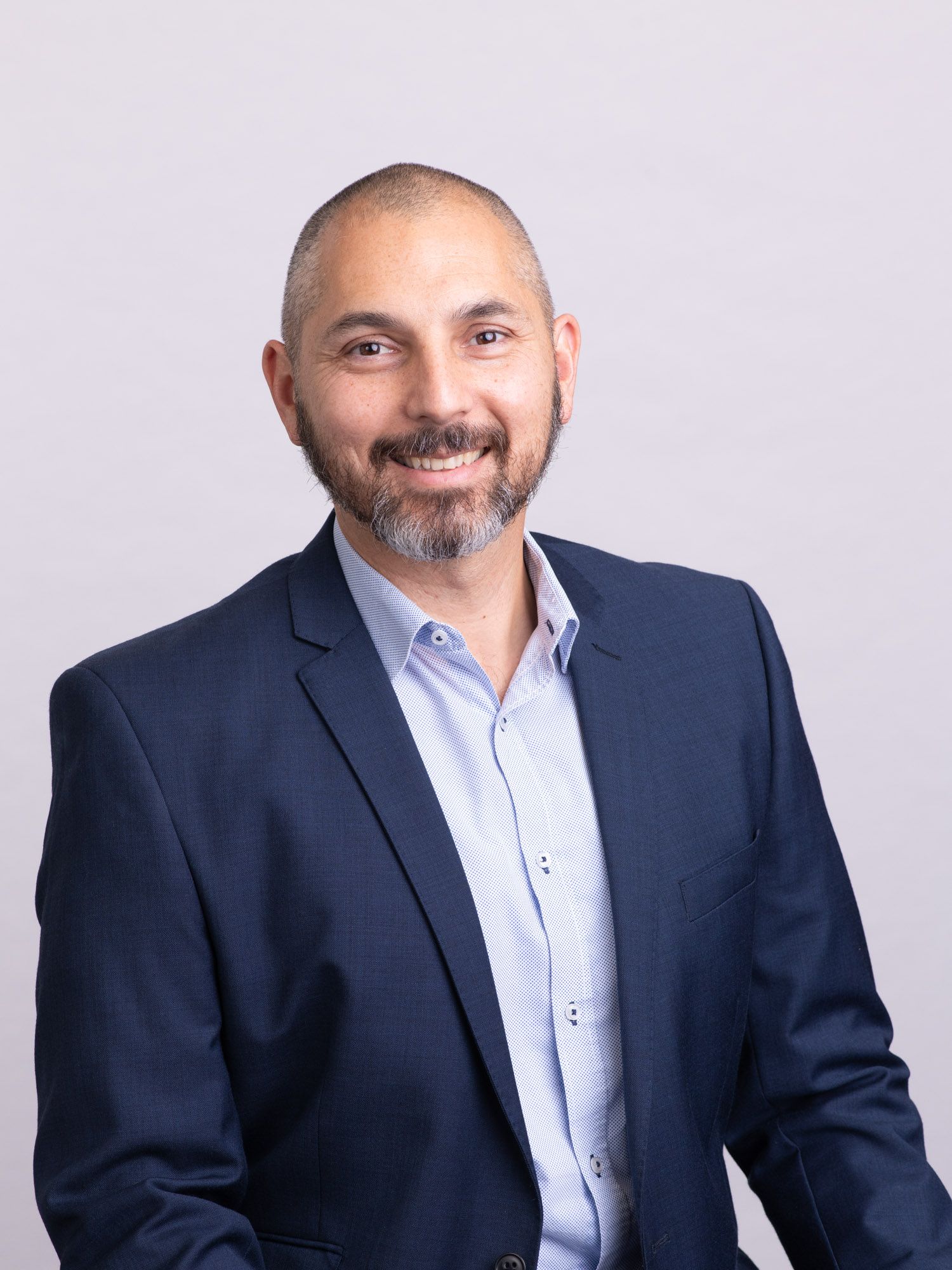 Professional headshot of a smiling middle-aged man with a beard wearing a navy blue blazer.